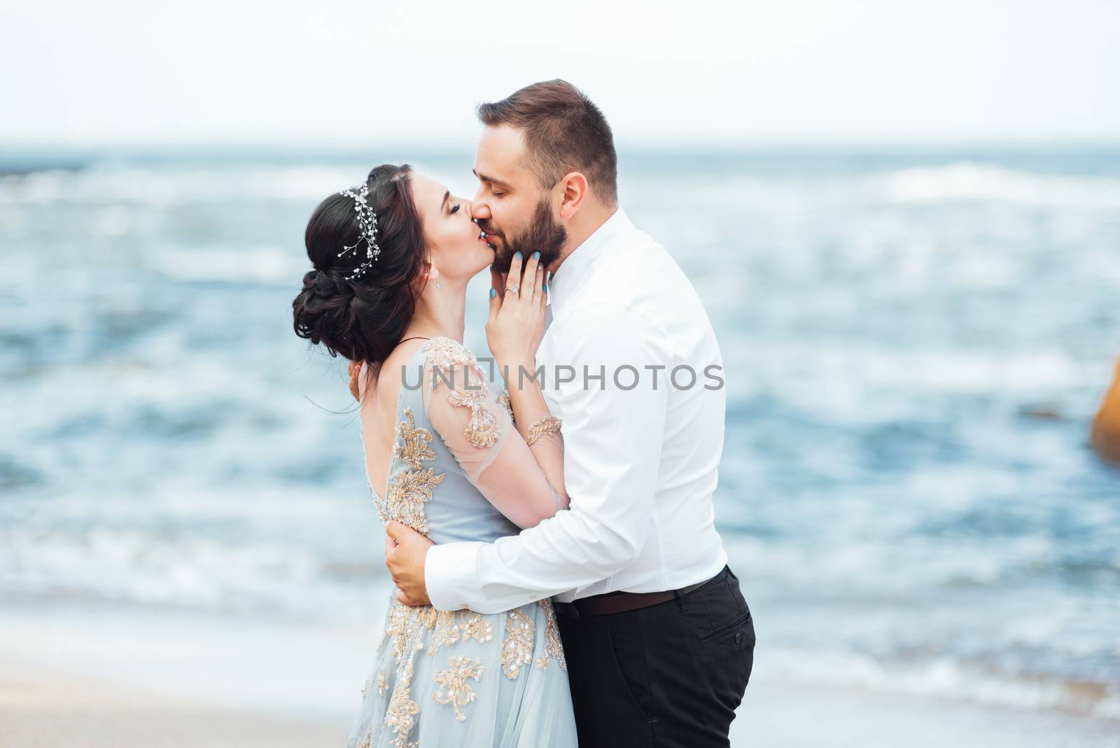 same couple with a bride in a blue dress walk along the ocean shore