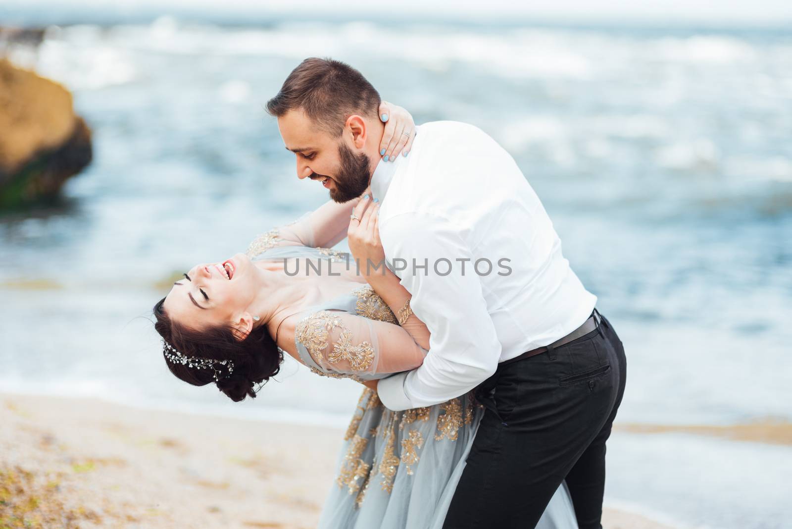 same couple with a bride in a blue dress walk along the ocean shore