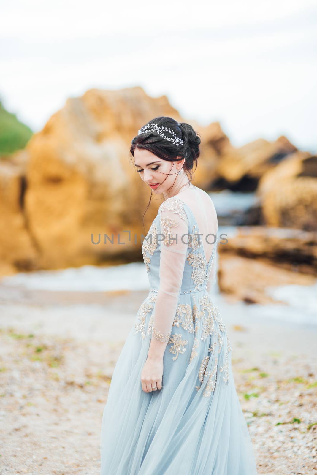 bride in a blue light dress walking along the ocean by Andreua