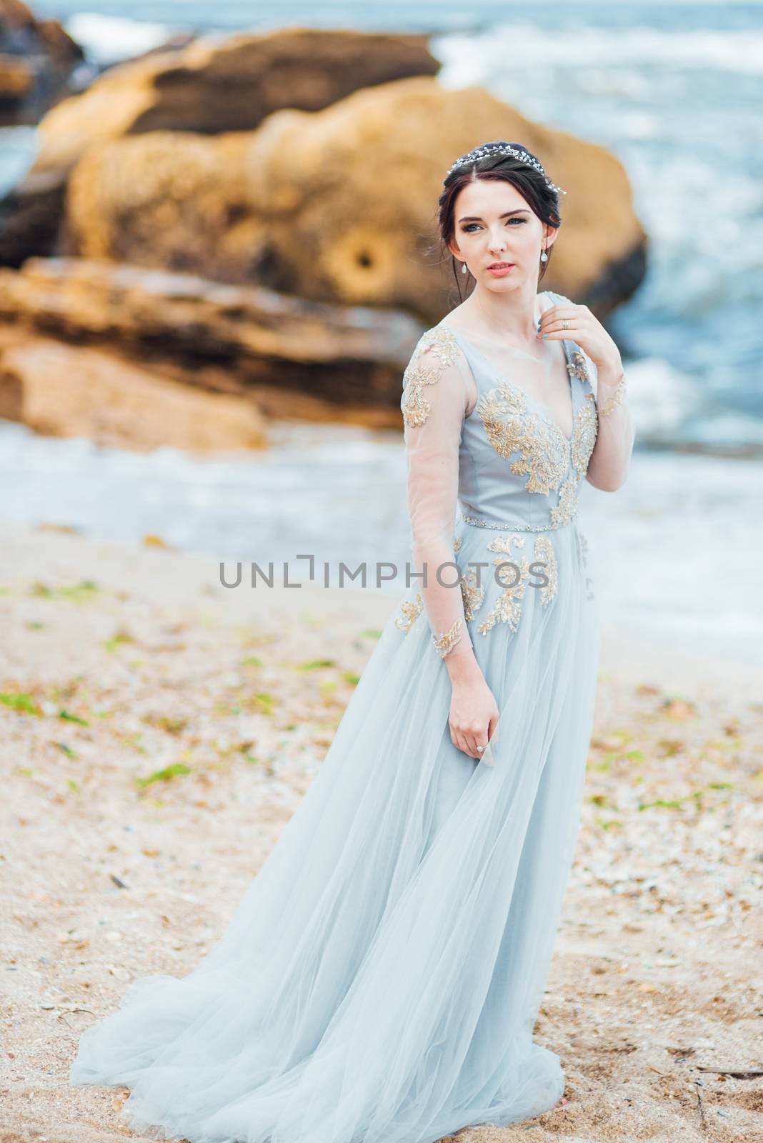 bride in a blue light dress walking along the ocean by Andreua