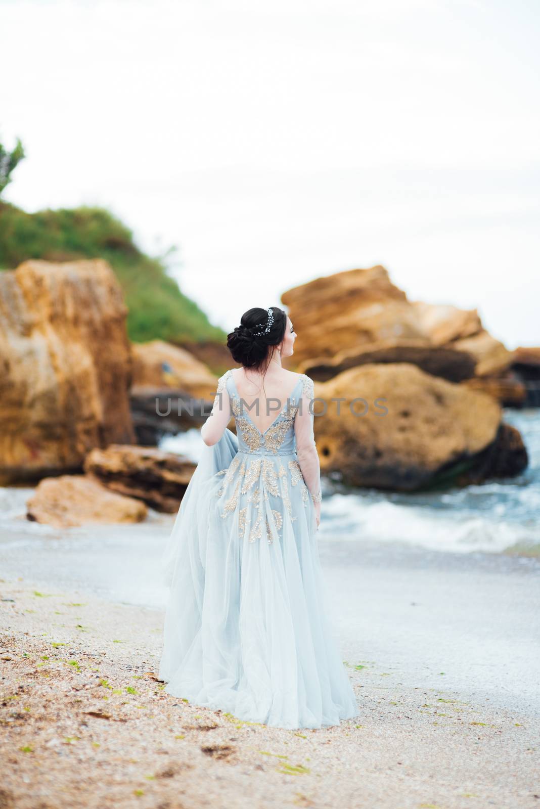 bride in a blue light dress walking along the ocean