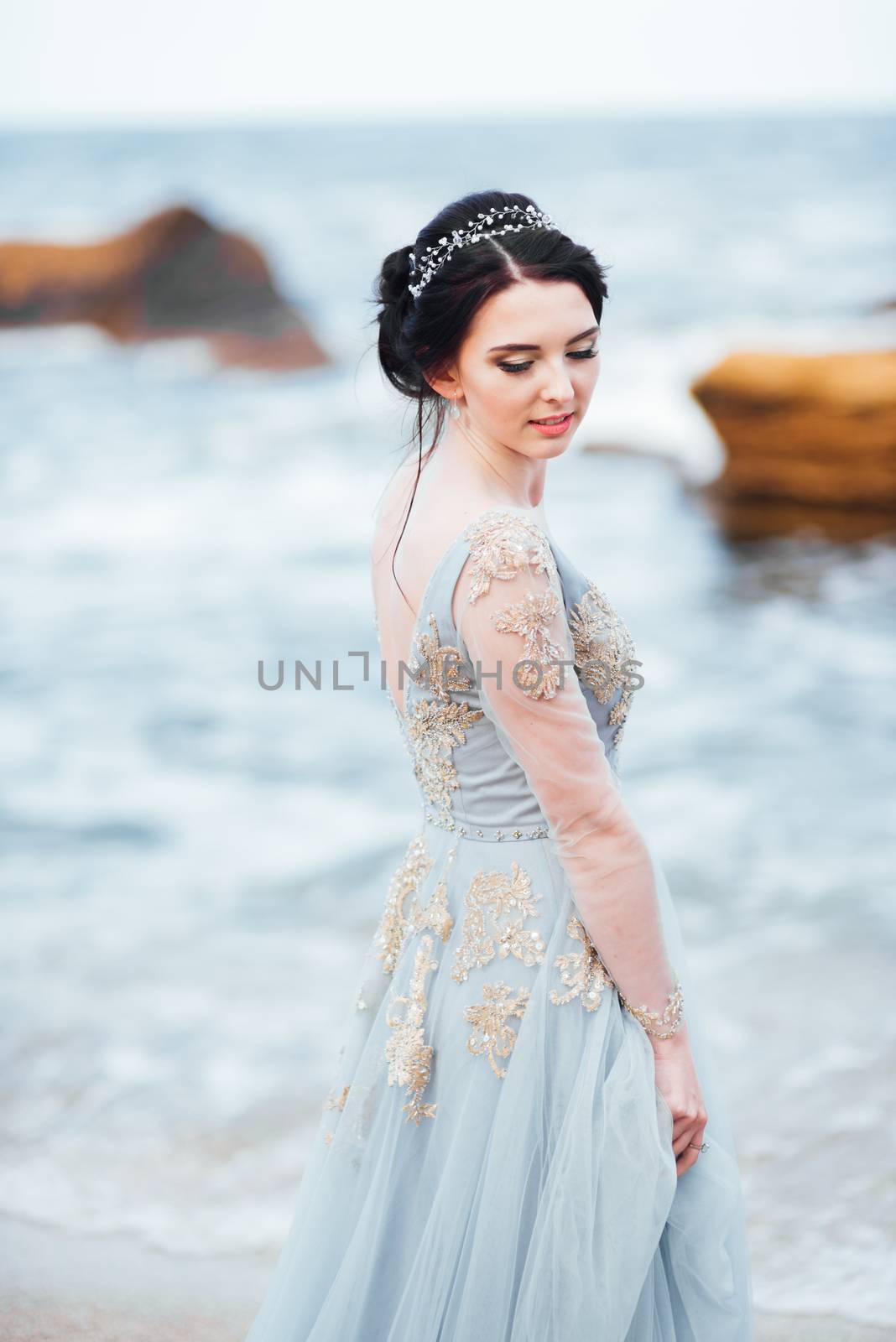 bride in a blue light dress walking along the ocean by Andreua
