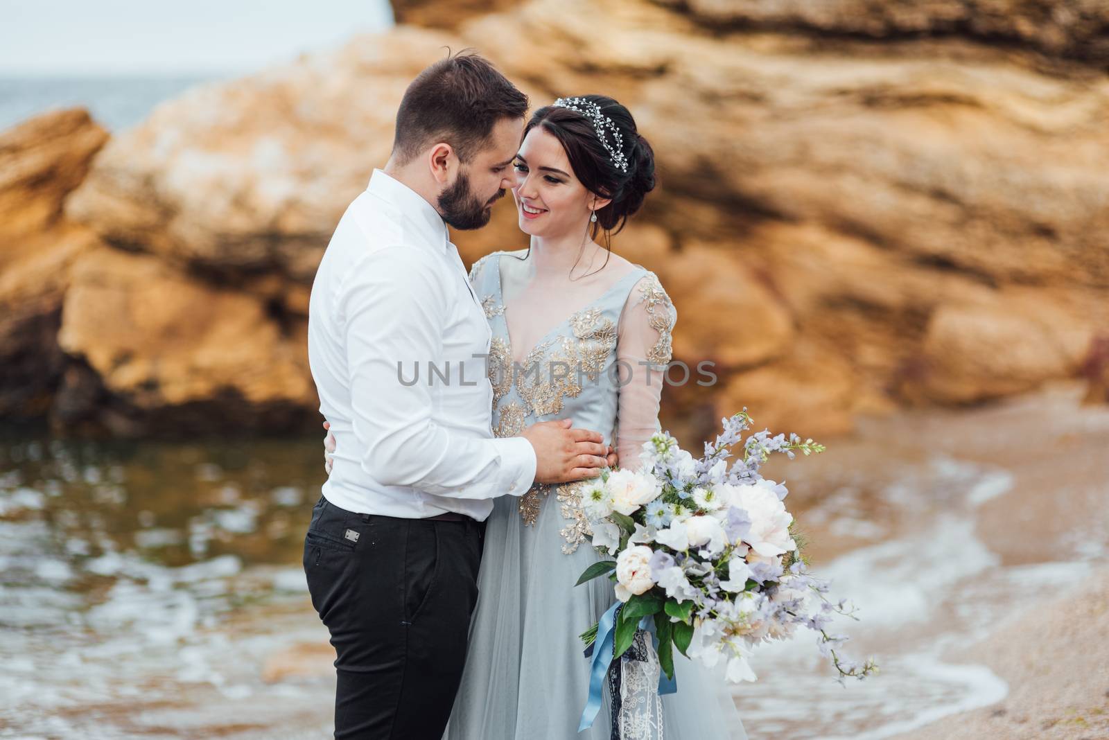 same couple with a bride in a blue dress walk along the ocean shore