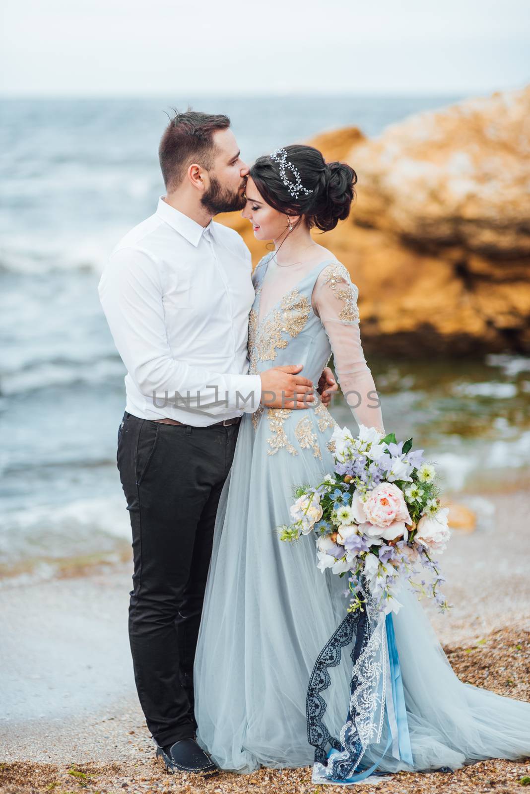 same couple with a bride in a blue dress walk along the ocean shore