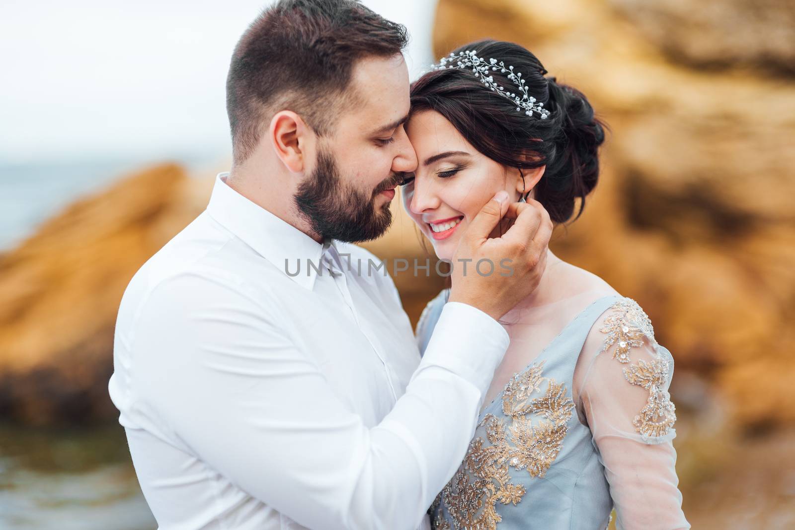 same couple with a bride in a blue dress walk along the ocean shore