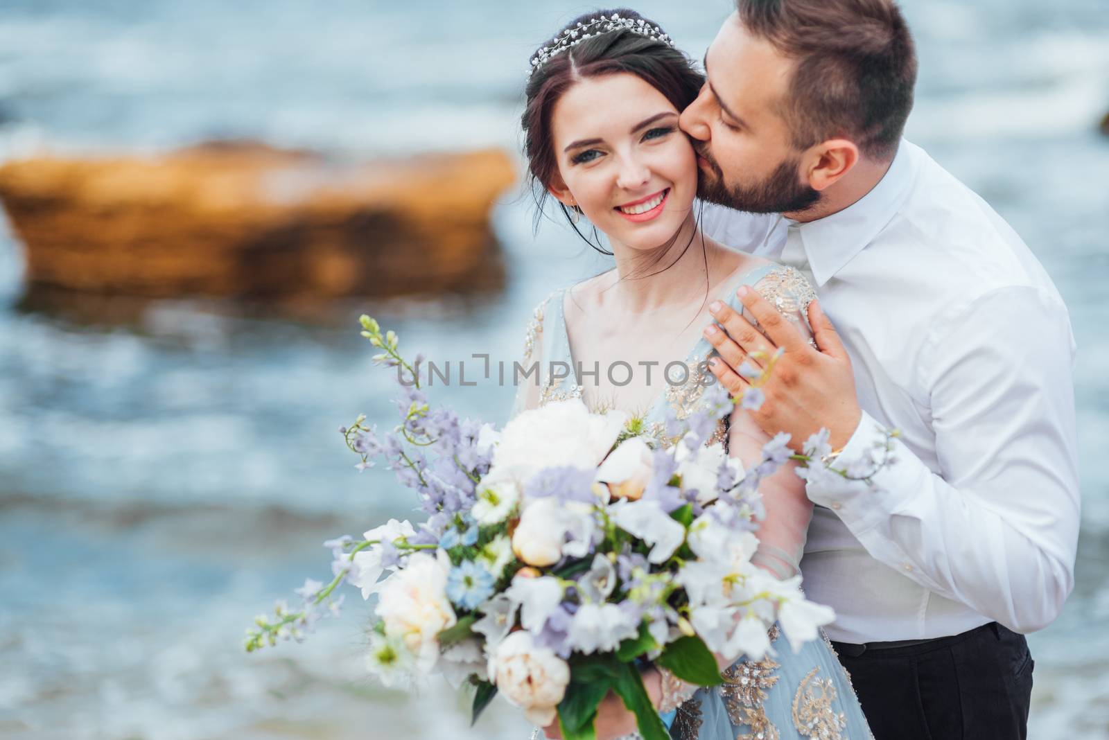 same couple with a bride in a blue dress walk along the ocean shore