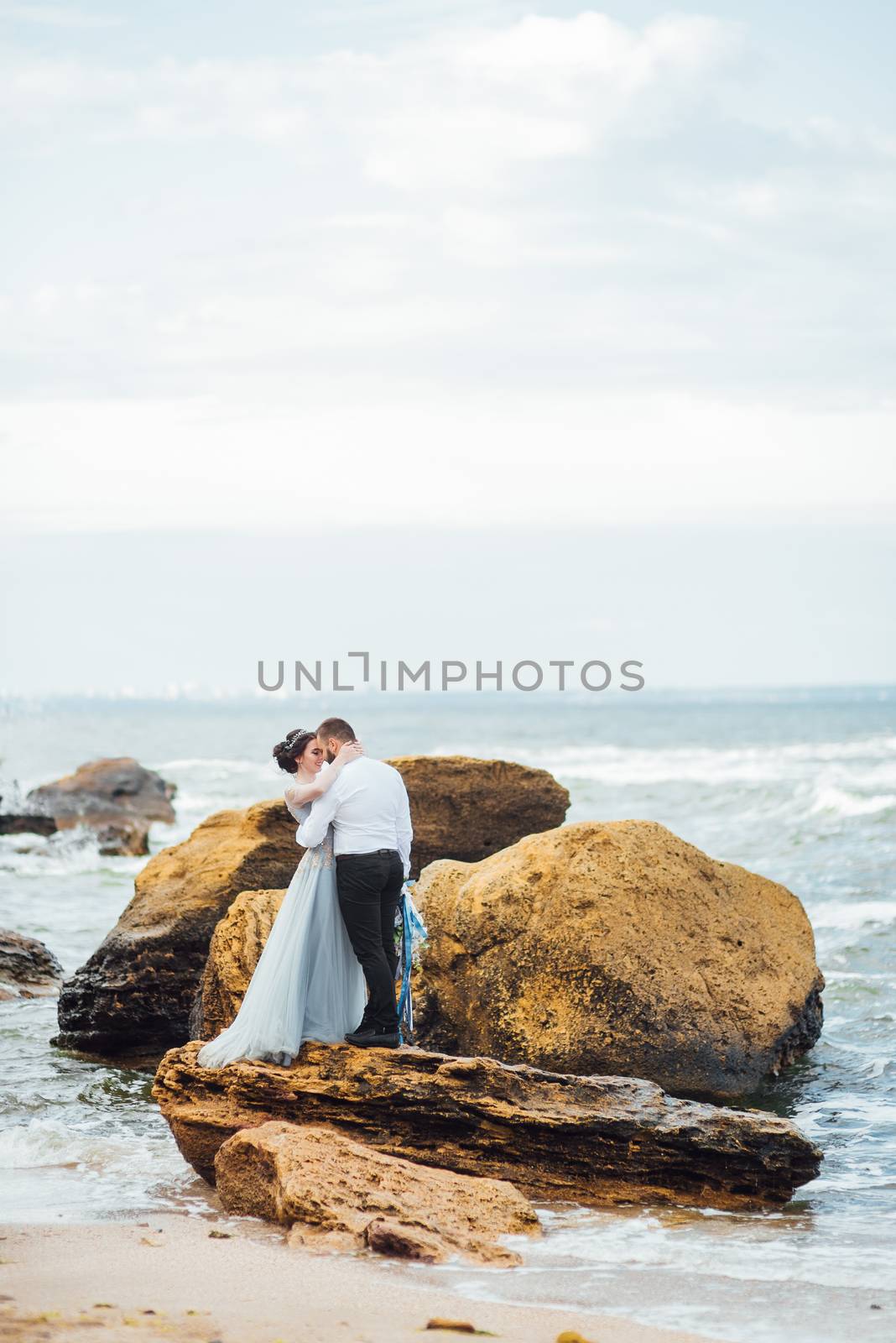 same couple with a bride in a blue dress walk along the ocean shore