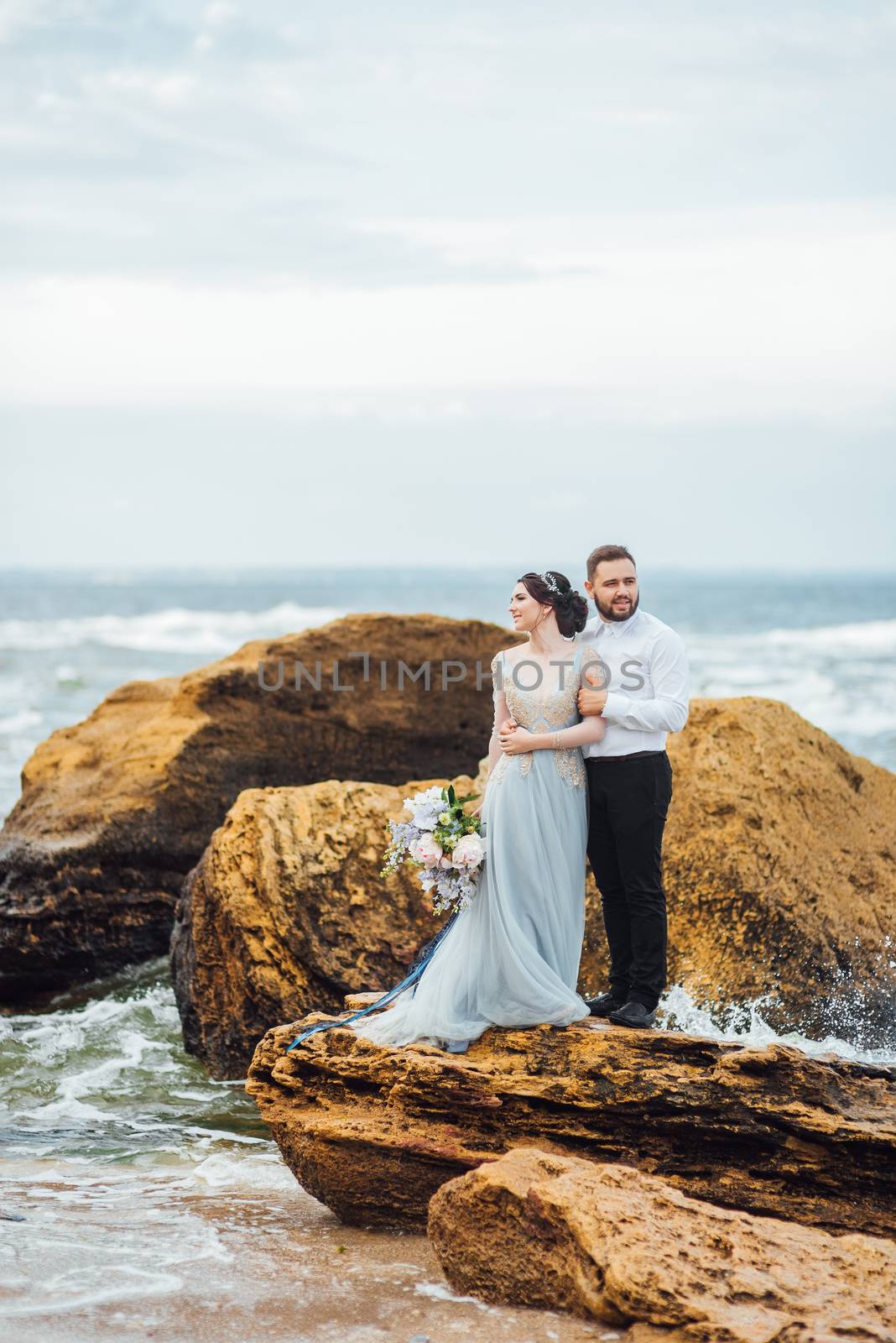 same couple with a bride in a blue dress walk along the ocean shore