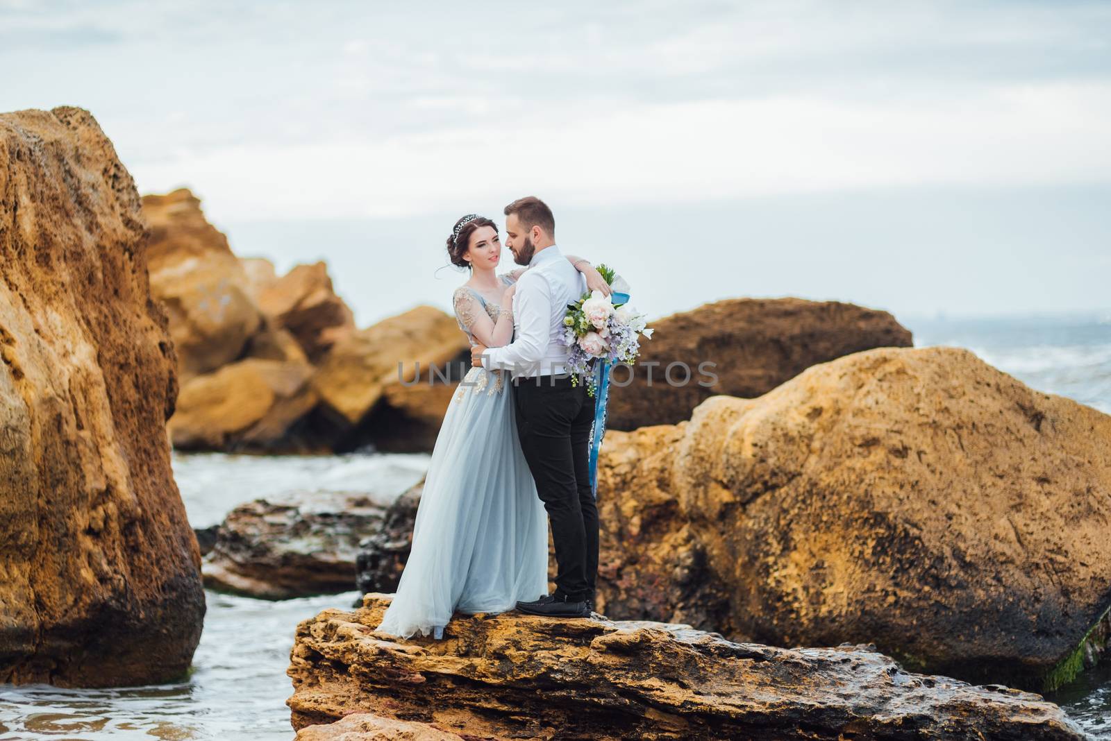 same couple with a bride in a blue dress walk along the ocean shore