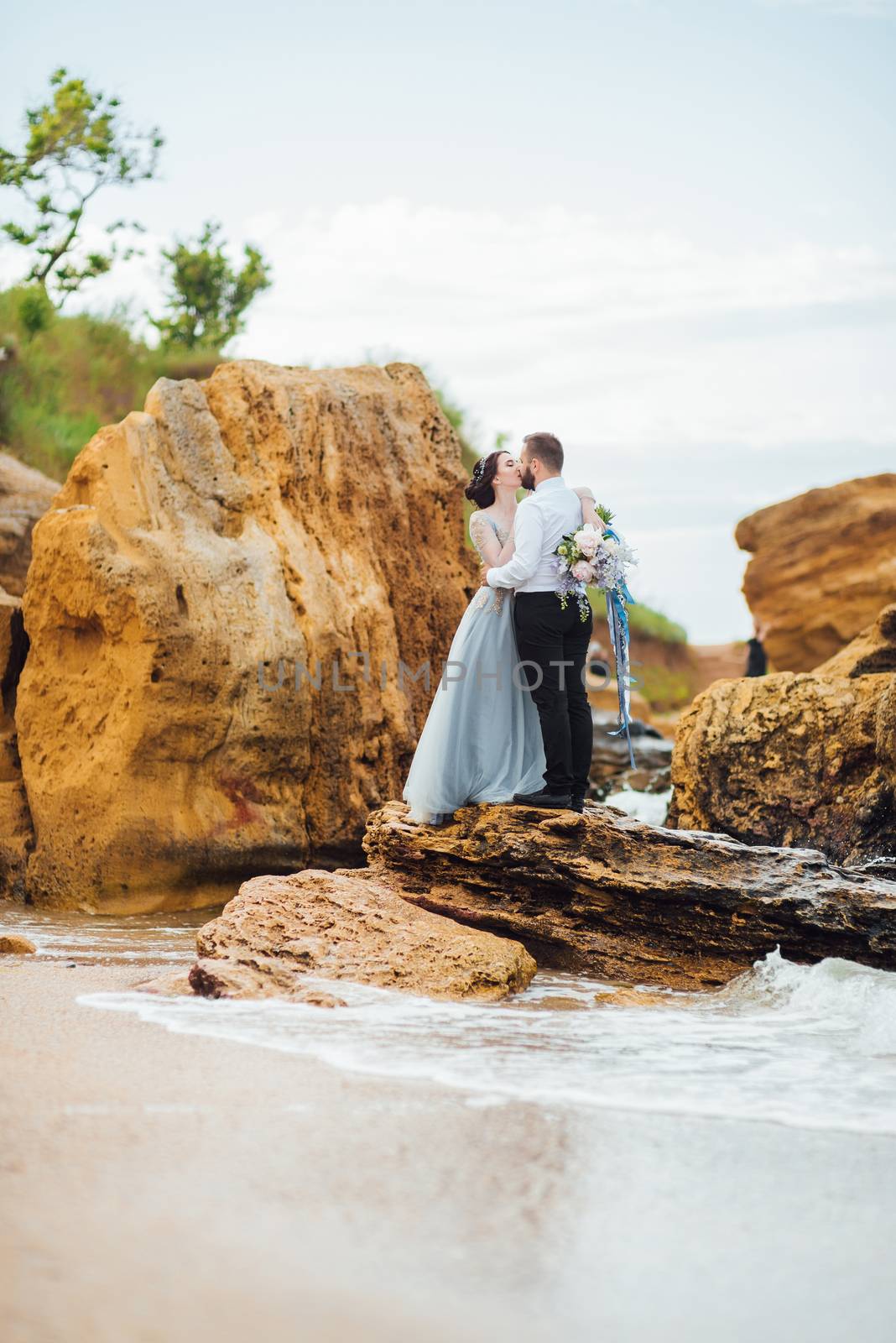 same couple with a bride in a blue dress walk along the ocean shore