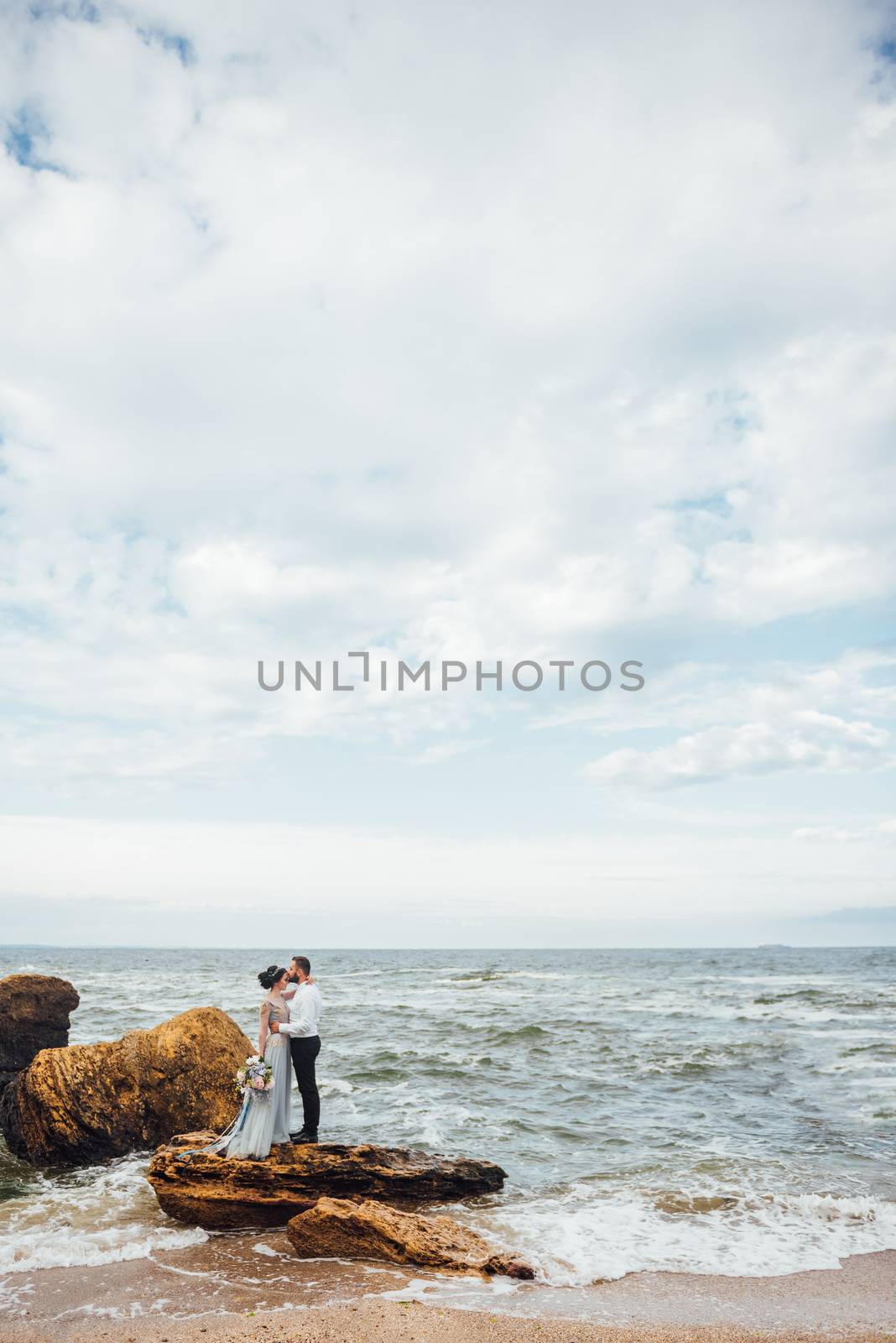 same couple with a bride in a blue dress walk along the ocean shore