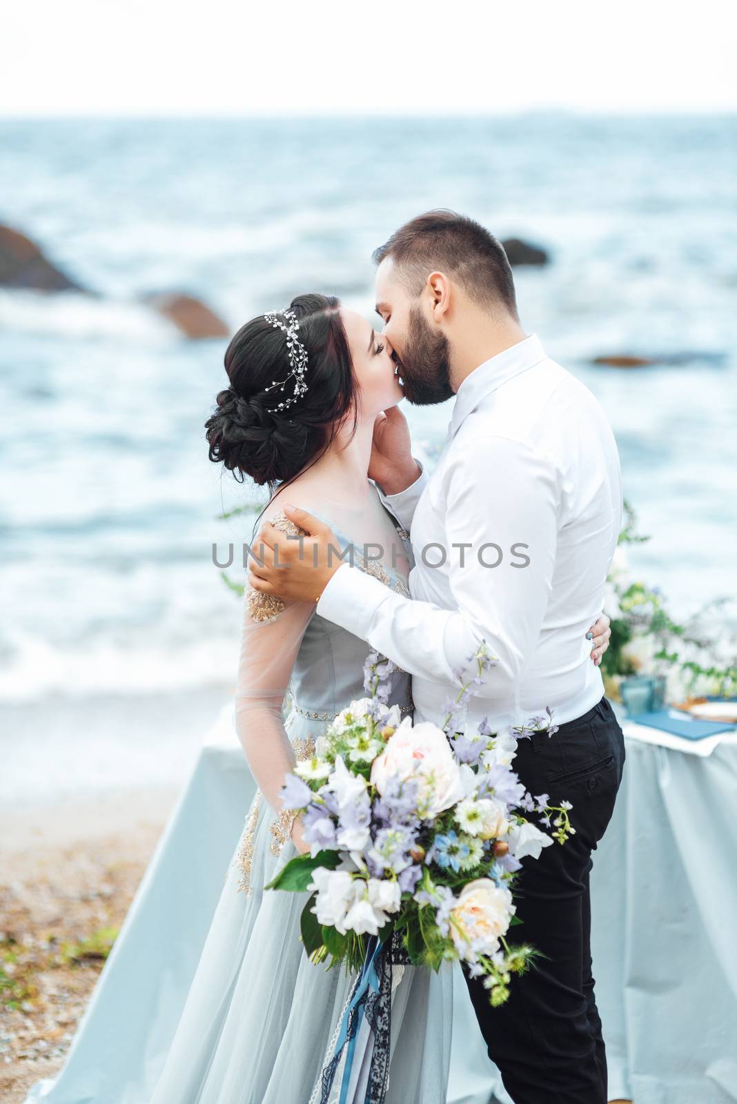 same couple with a bride in a blue dress walk along the ocean shore