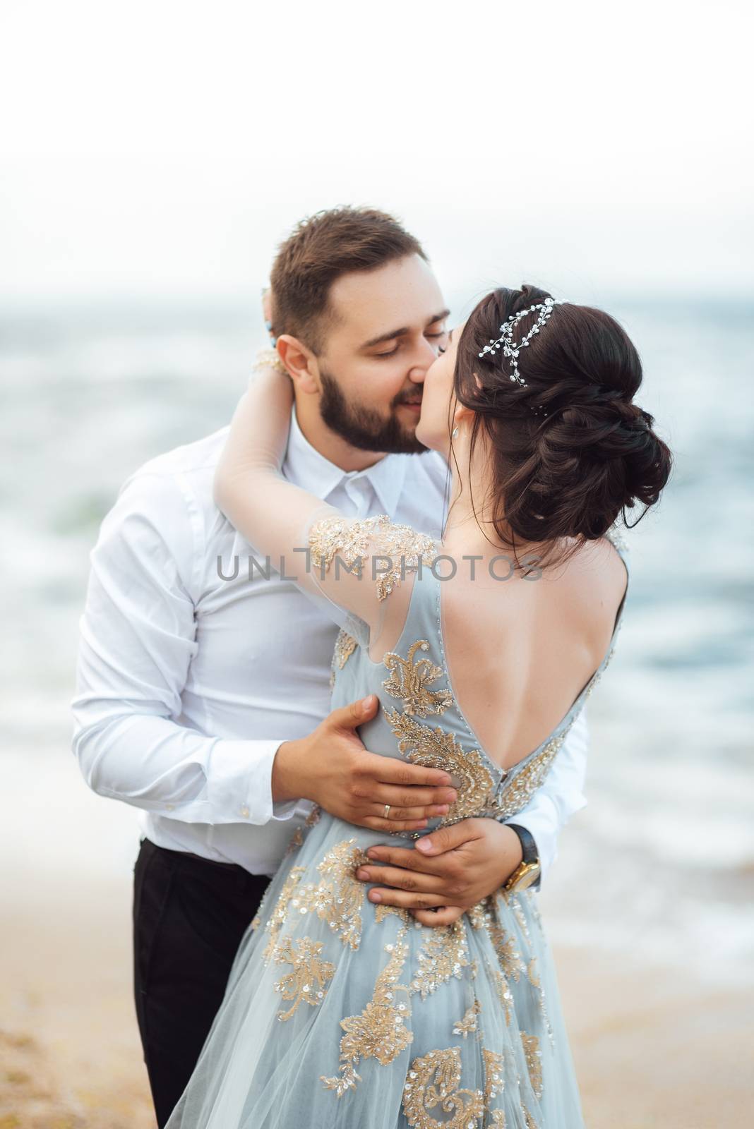 same couple with a bride in a blue dress walk along the ocean shore