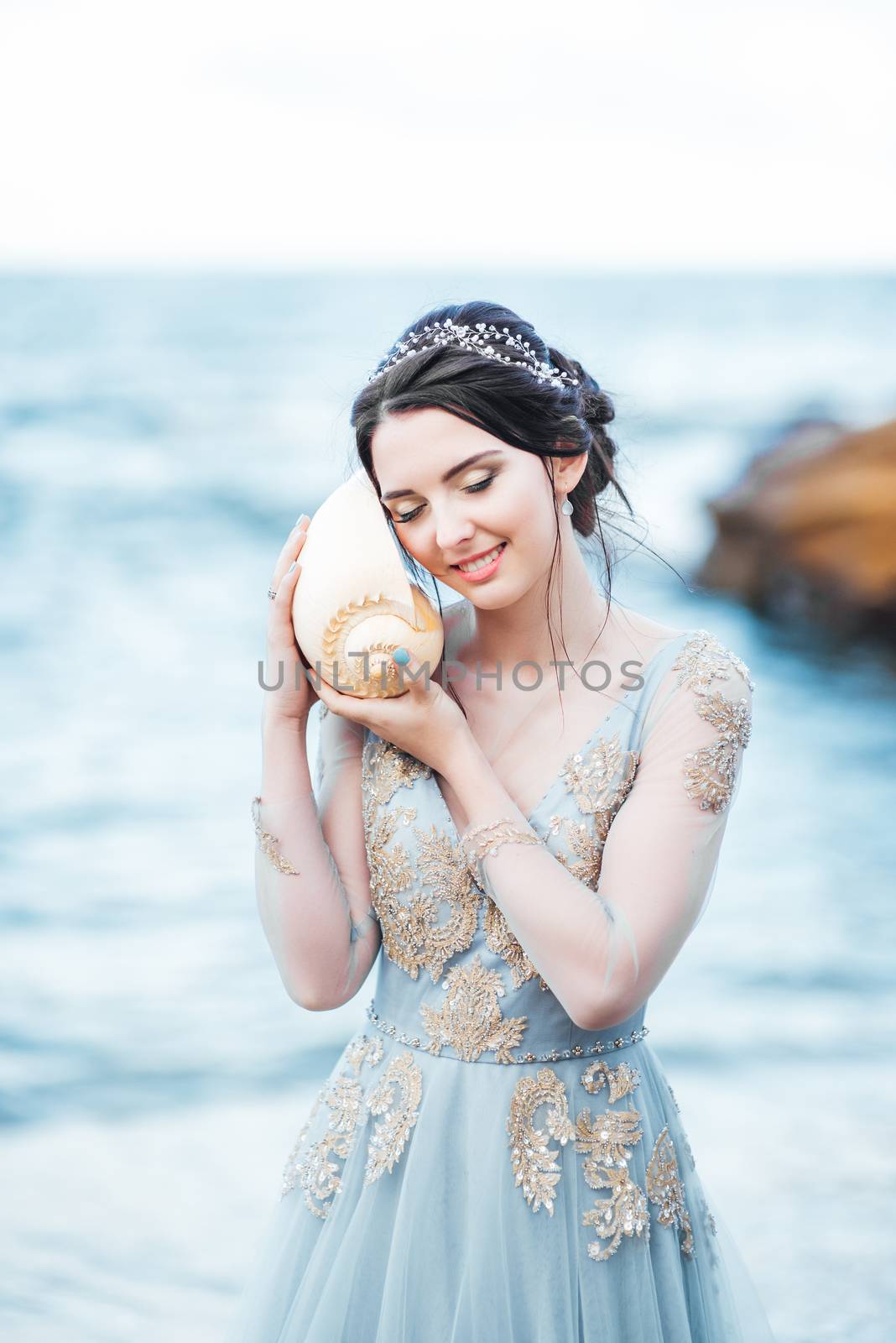 bride with a big shell on the beach in a blue wedding dress