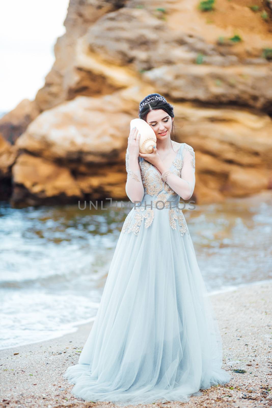 bride with a big shell on the beach in a blue wedding dress