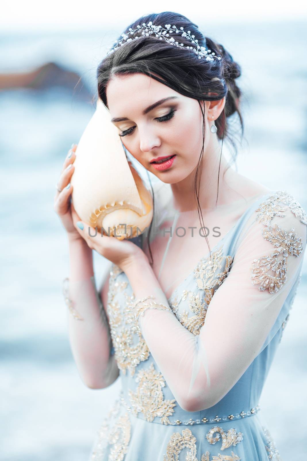 bride with a big shell on the beach in a blue wedding dress