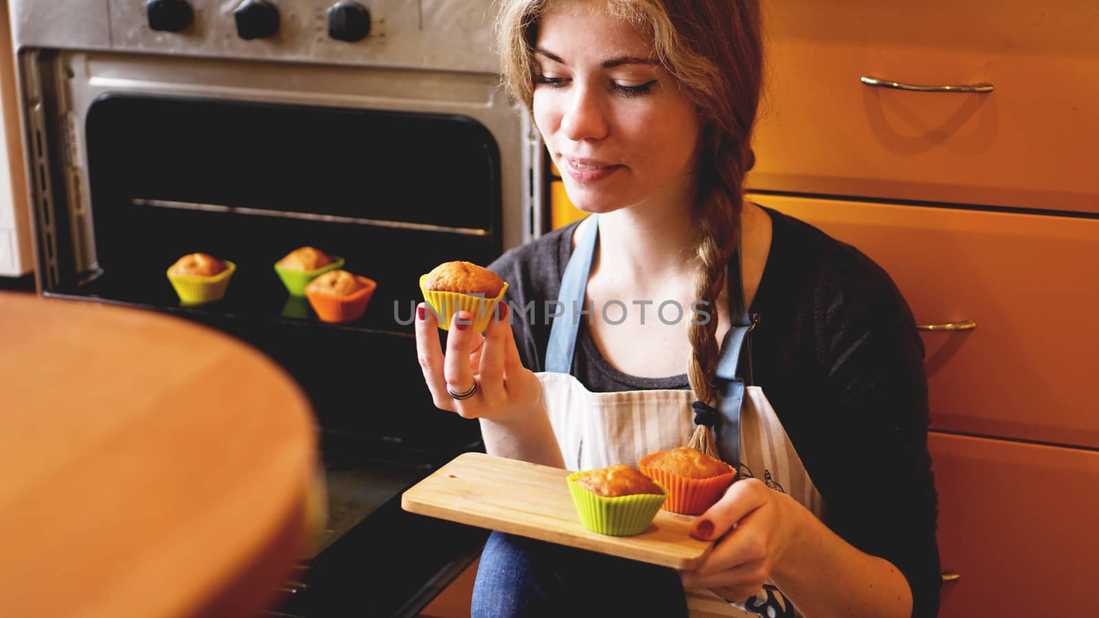 Beautiful blonde woman showing muffins in a kitchen. Cooking and home concept