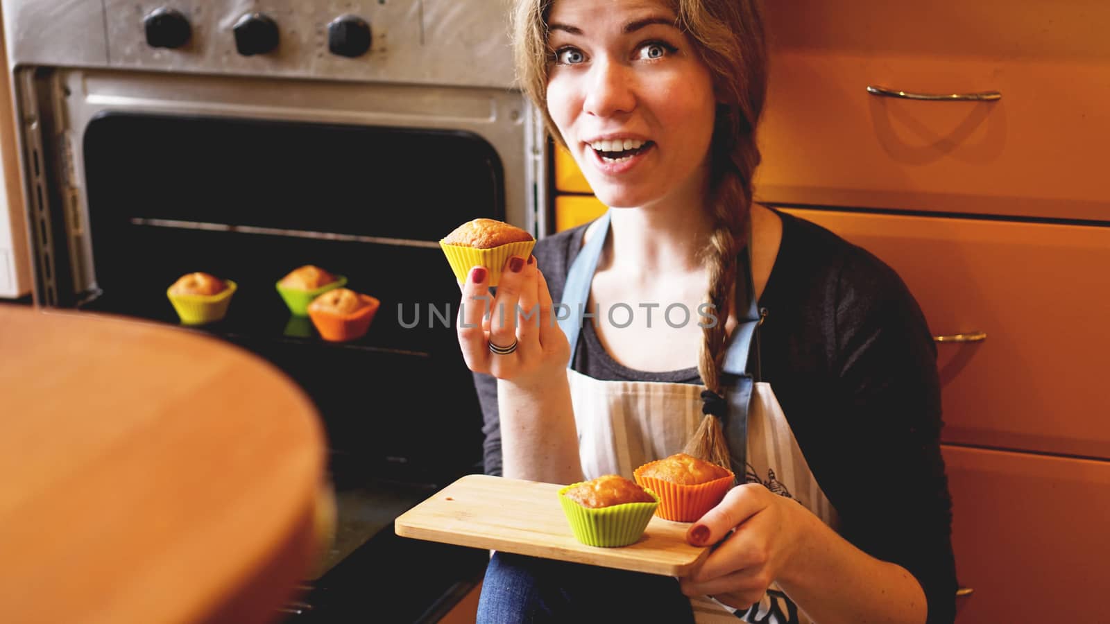 Beautiful blonde woman showing muffins in a kitchen by natali_brill