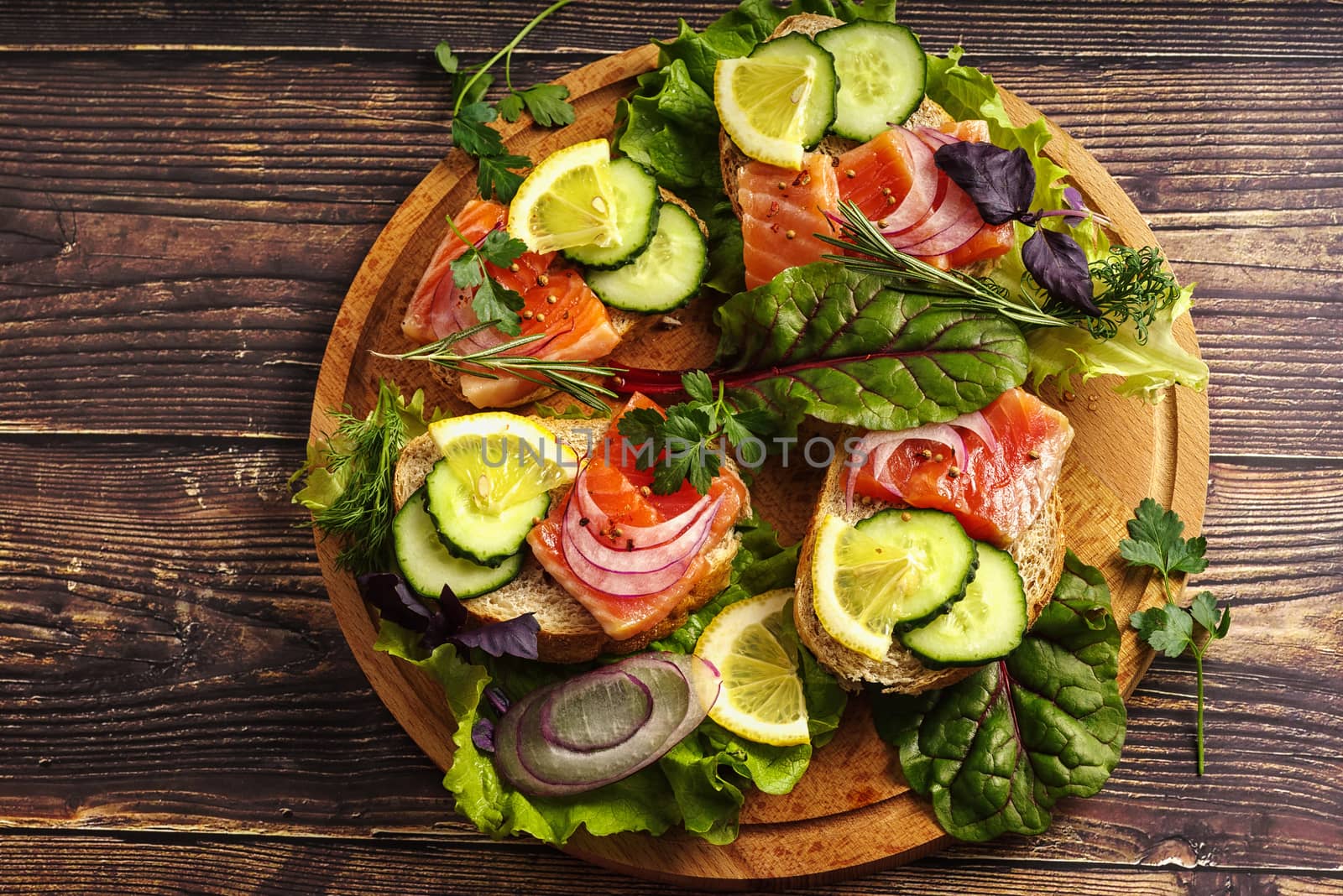 Salmon sandwich with greens, red onions and spices on a wooden table.