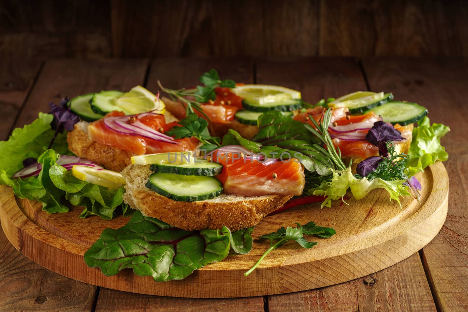 Salmon sandwich with greens, red onions and spices on a wooden table.