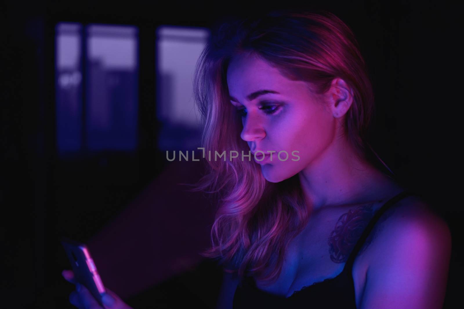 Girl using cellphone at night with neon light - pink and blue