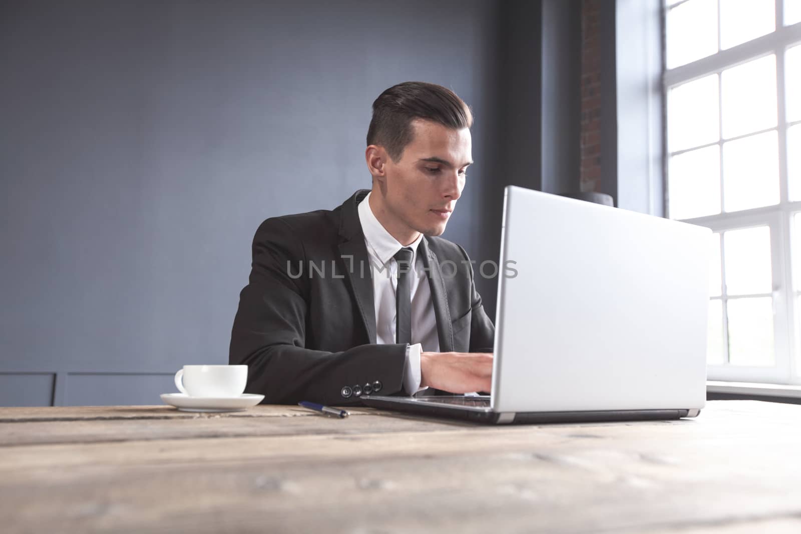 Young businessman in black suit using laptop in office