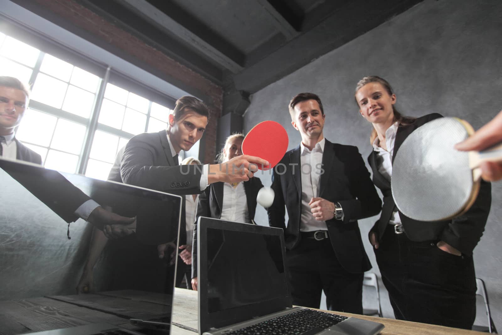 Business people play ping pong on office table with laptops