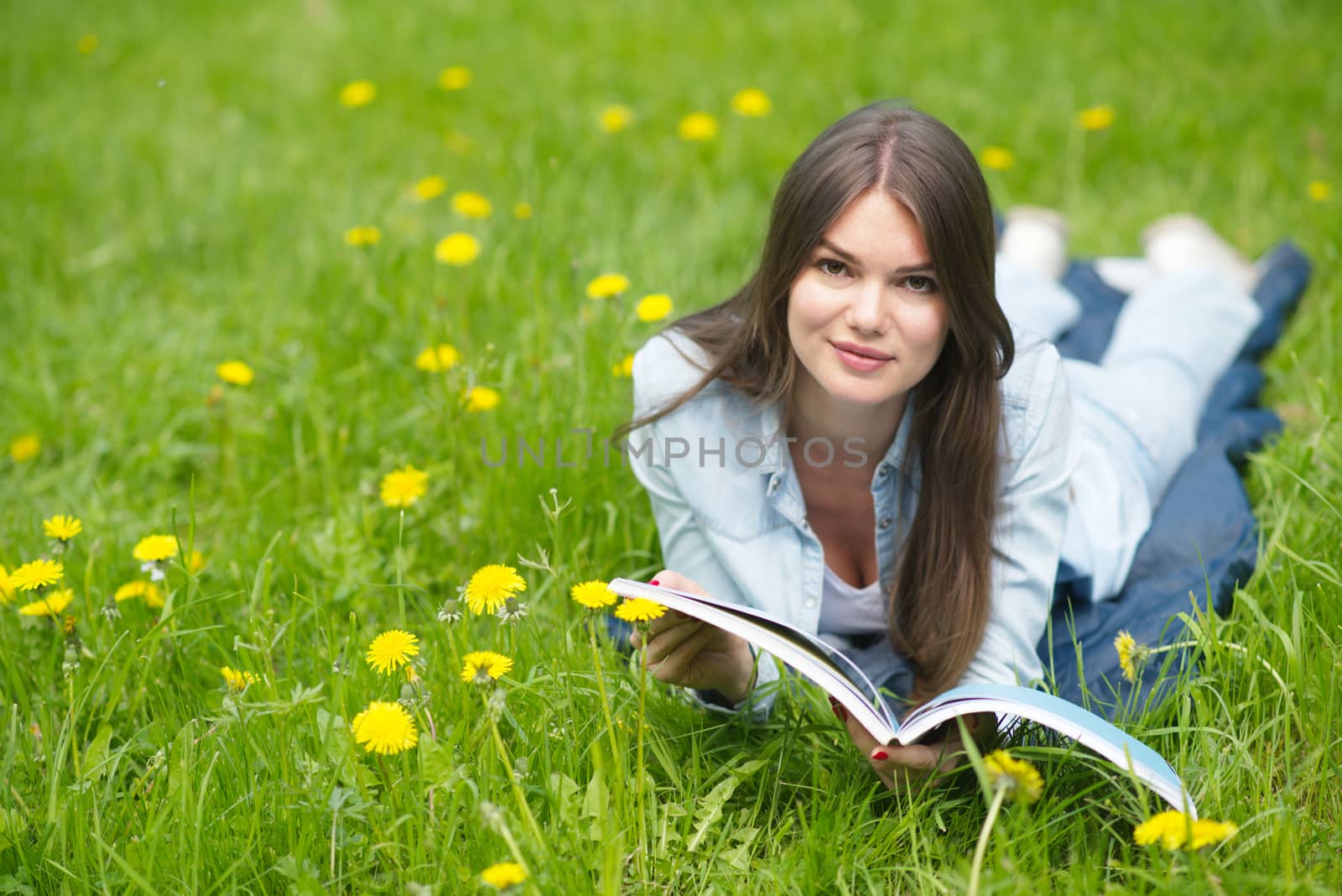 A young brunette woman lying on the grass outdoors with a magazine