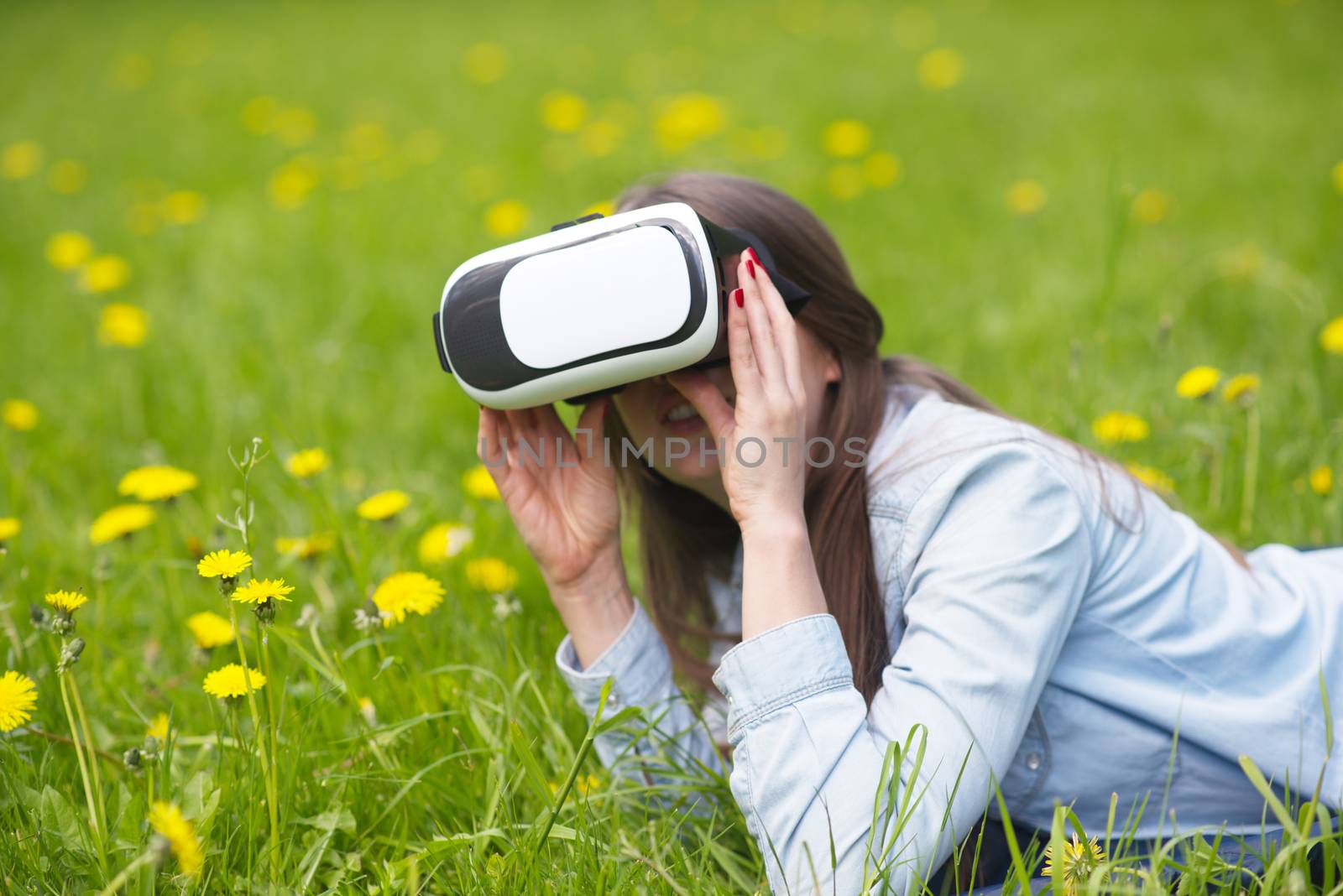 Woman using the virtual reality headset outdoors laying in spring flower field