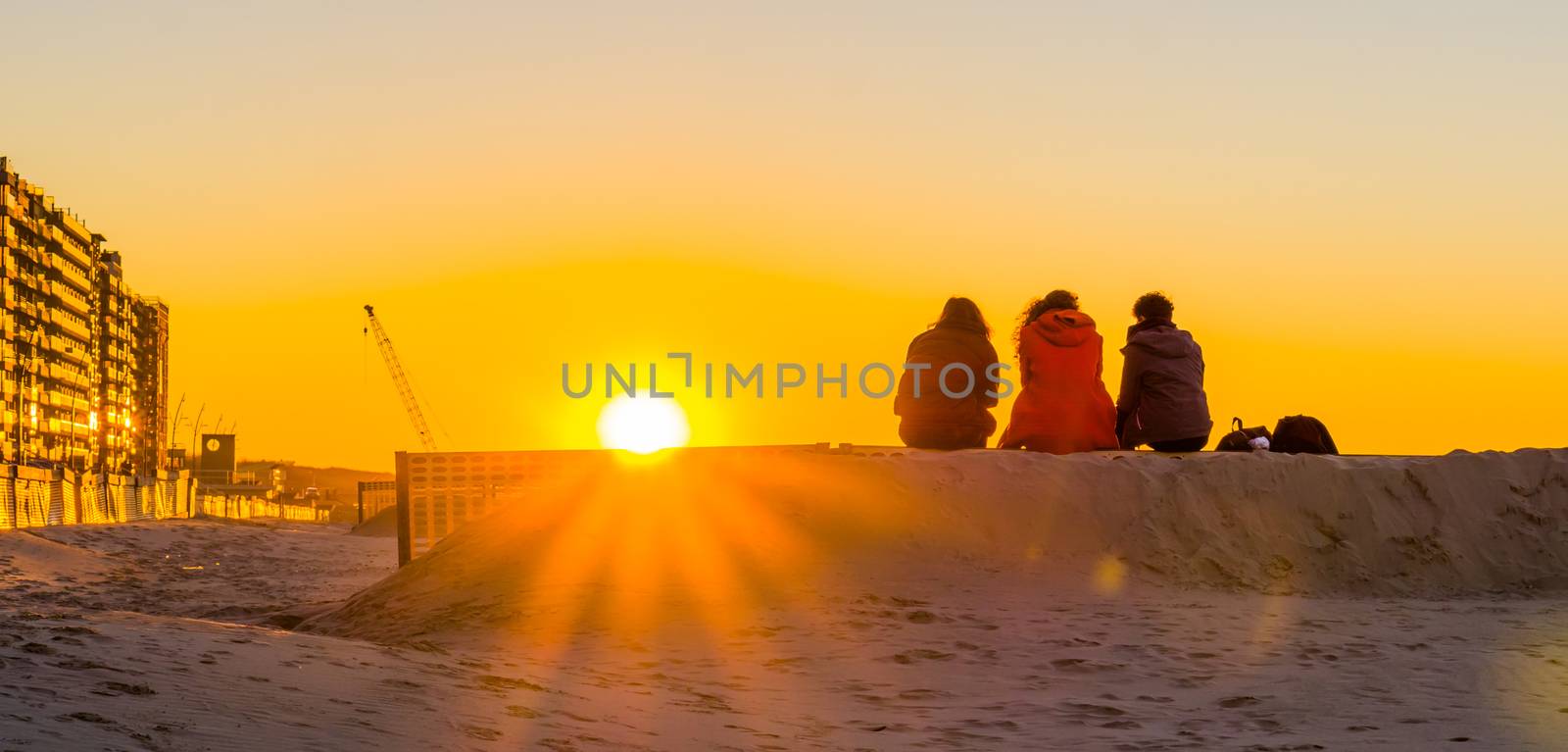 three teenagers sitting on a sand hill together, watching and enjoying the sunset at the beach, young people in nature by charlottebleijenberg