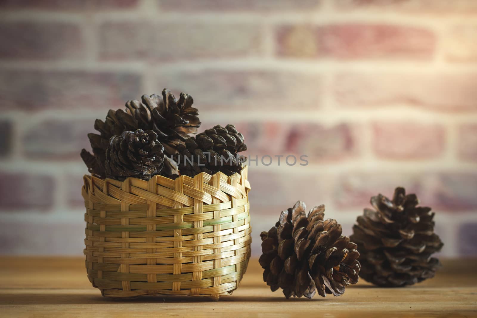 Pine Cone in bamboo basket on wooden table and brick wall backgr by SaitanSainam