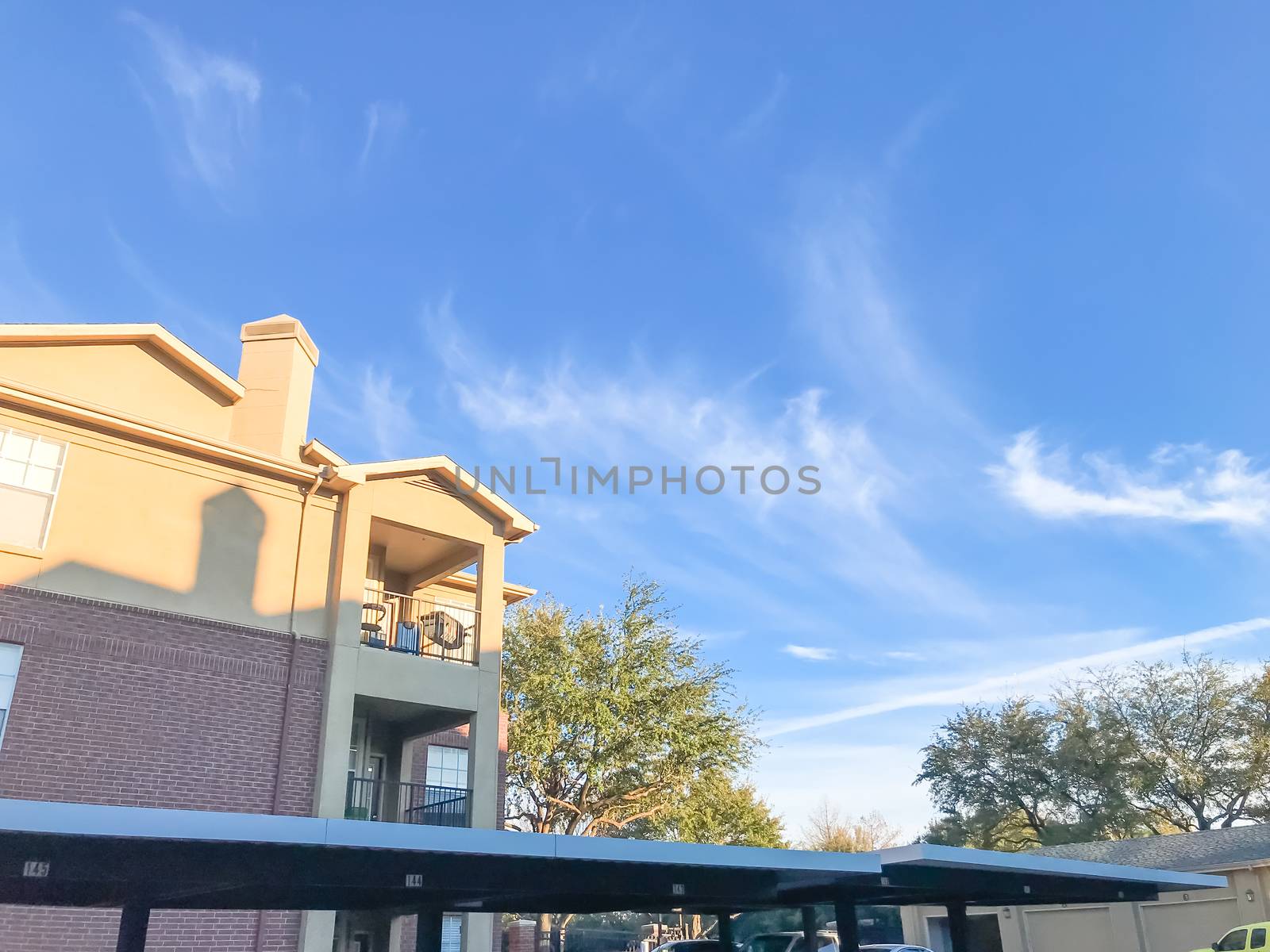 Typical apartment building complex in Lewisville, Texas, USA. Low angle view of multi-stories rental real estate with covered parking at sunset with cloud sky