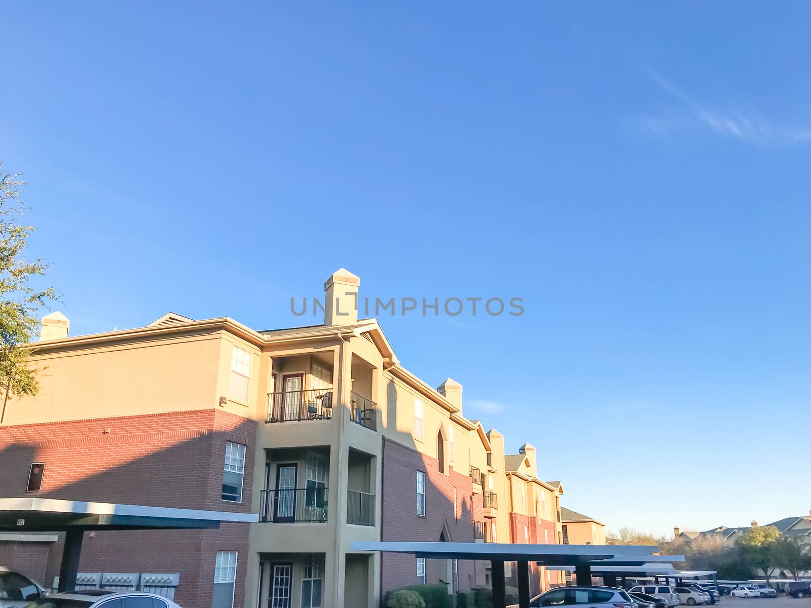 Apartment building complex and parked cars in Lewisville, Texas, USA. Low angle view of multi-stories rental real estate with covered parking at sunset with cloud sky