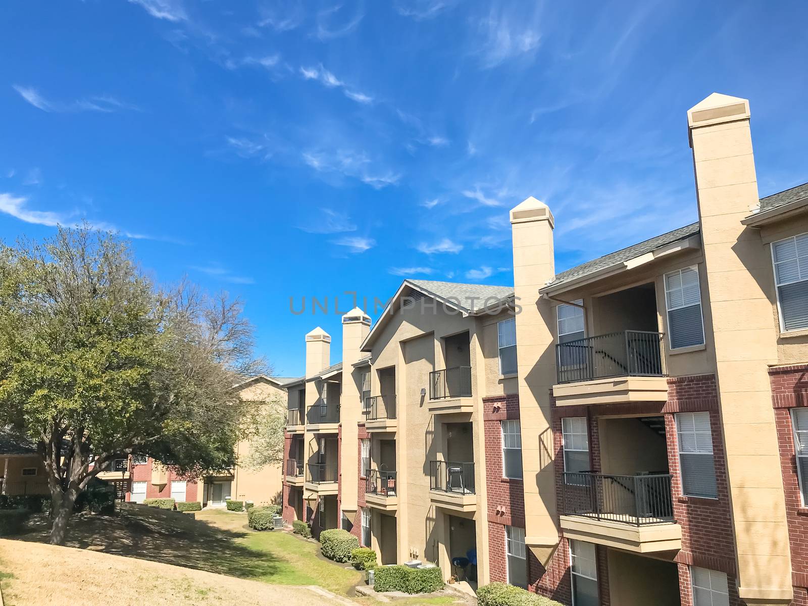 Typical apartment complex building with hillside backyard in Lewisville, Texas, USA. Sunny spring day with blue sky and white clouds over high chimney