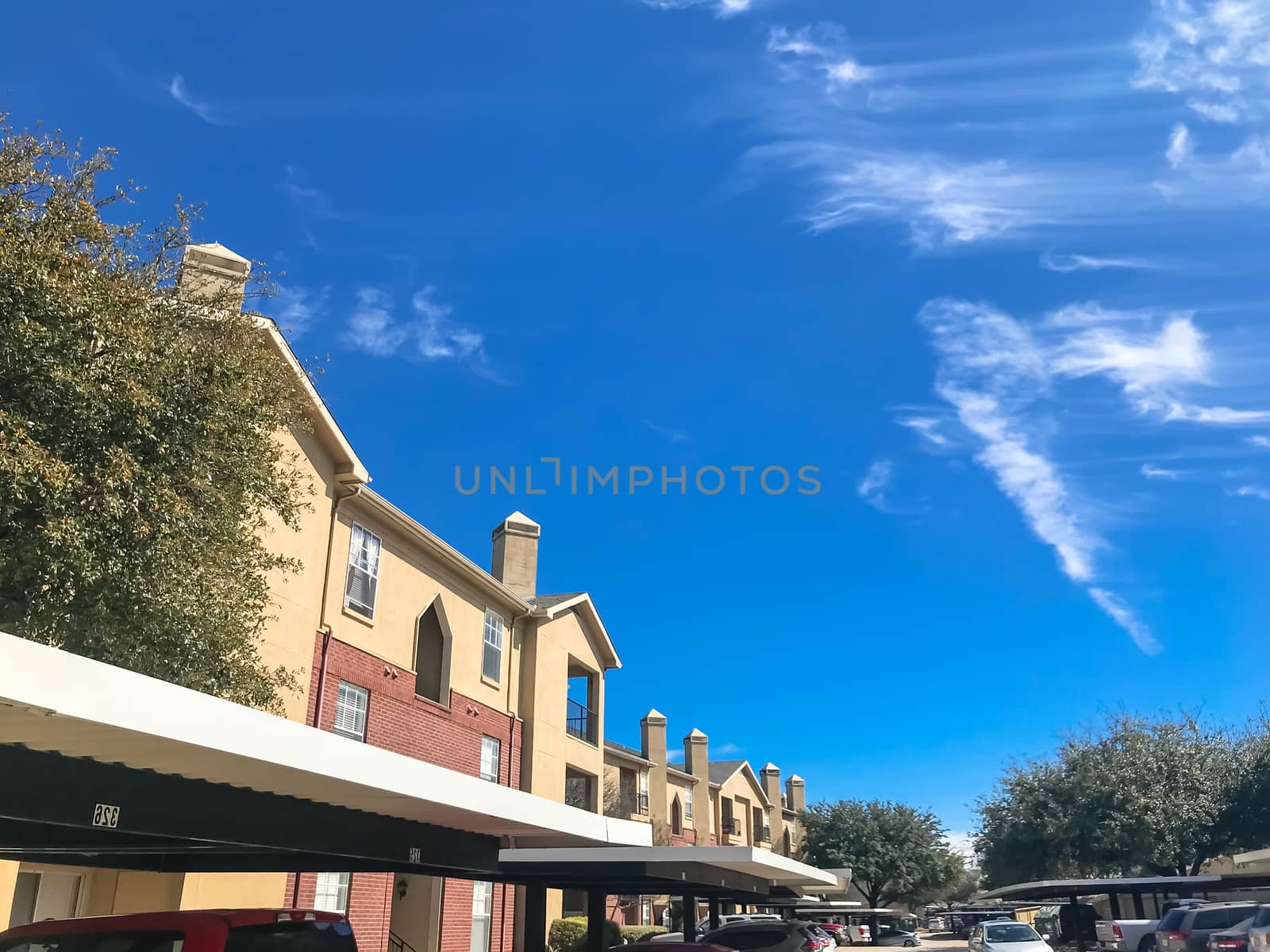 Lew angle view typical apartment building complex with covered parking in Lewisville, Texas, USA. Sunny spring day with blue sky and white clouds over tall chimney