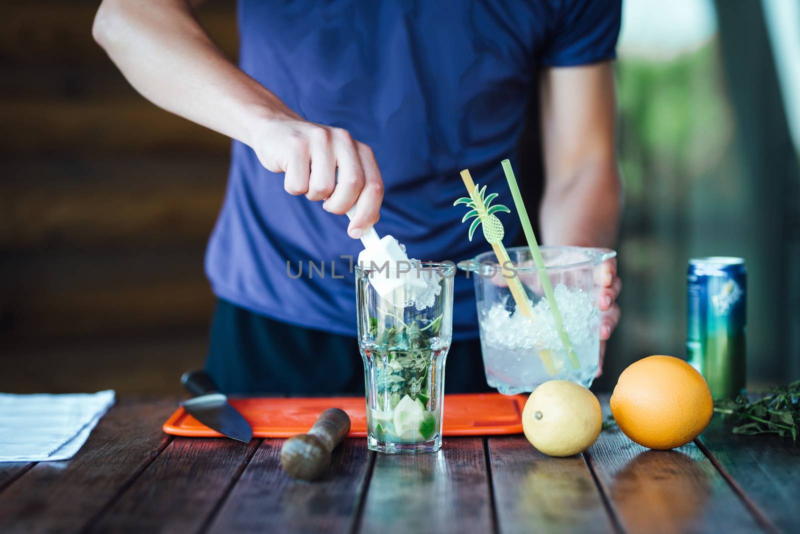 Barman prepares fruit alcohol cocktail based on lime, mint, orange, soda and alcohol