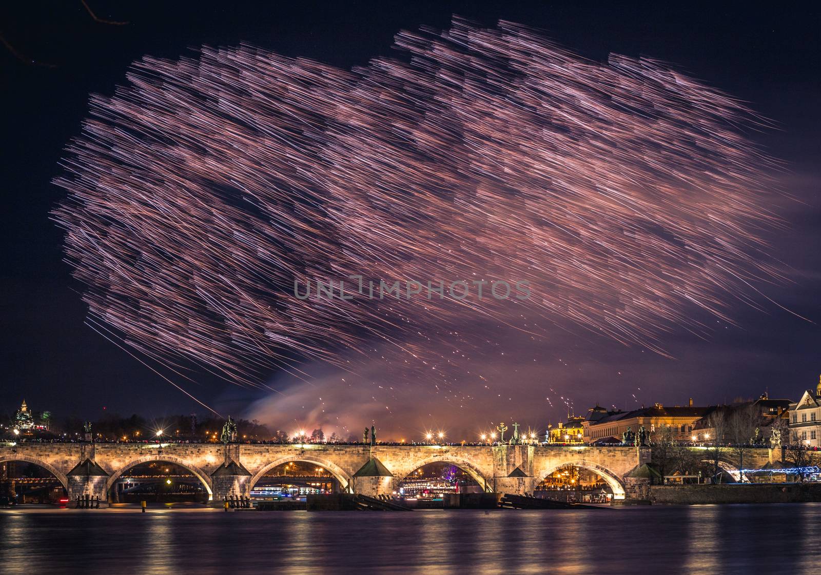 A fireworks show is staged near the historical Charles Bridge in the centre of Prague, with reflections in water.