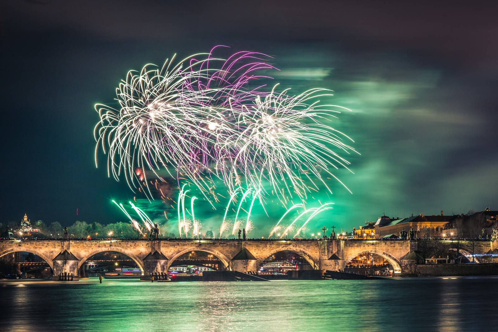 A fireworks show is staged near the historical Charles Bridge in the centre of Prague, with reflections in water.