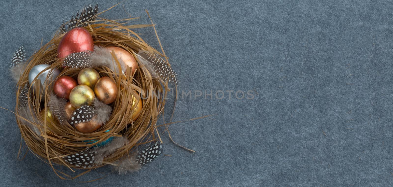 Happy Easter holiday greeting symbol stylish natural wooden grass nest with colorful quail eggs and feathers on gray fabric background