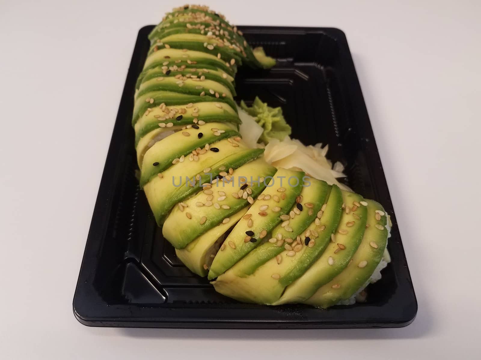 Japanese sushi with avocado and rice in black plastic container on white surface