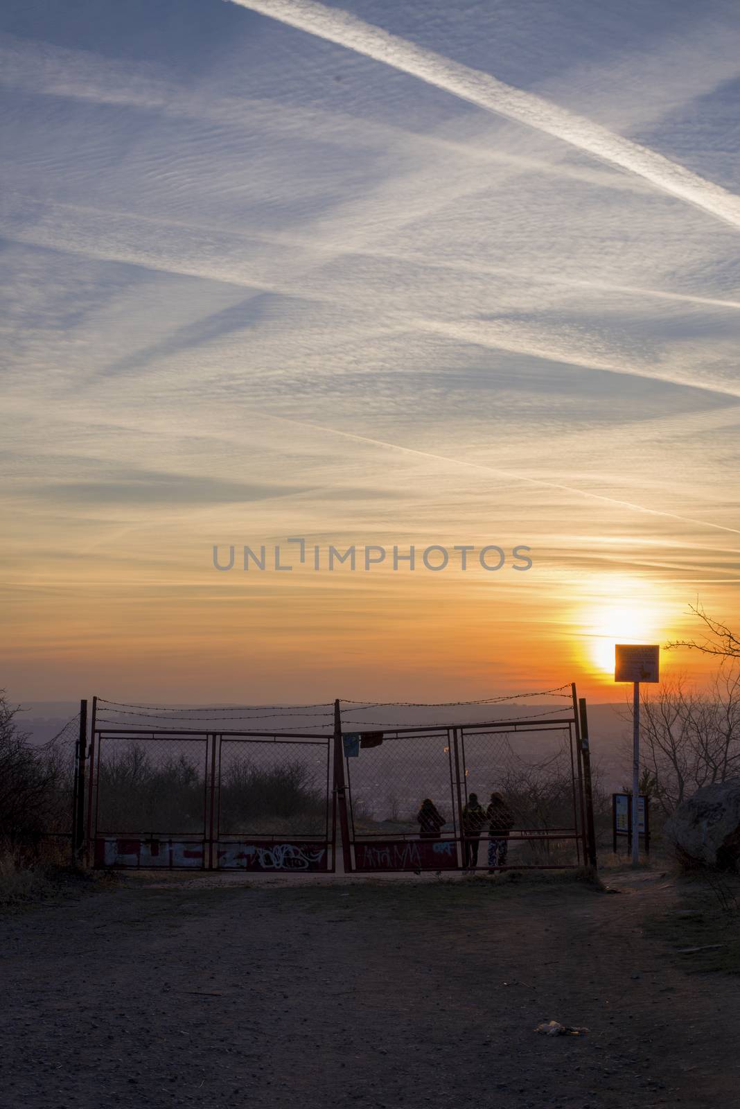 Unidentifiable People behind an old gate. Illegal trespassing scene with sunset sky and jet railwayas mark on the sky by vladiczech