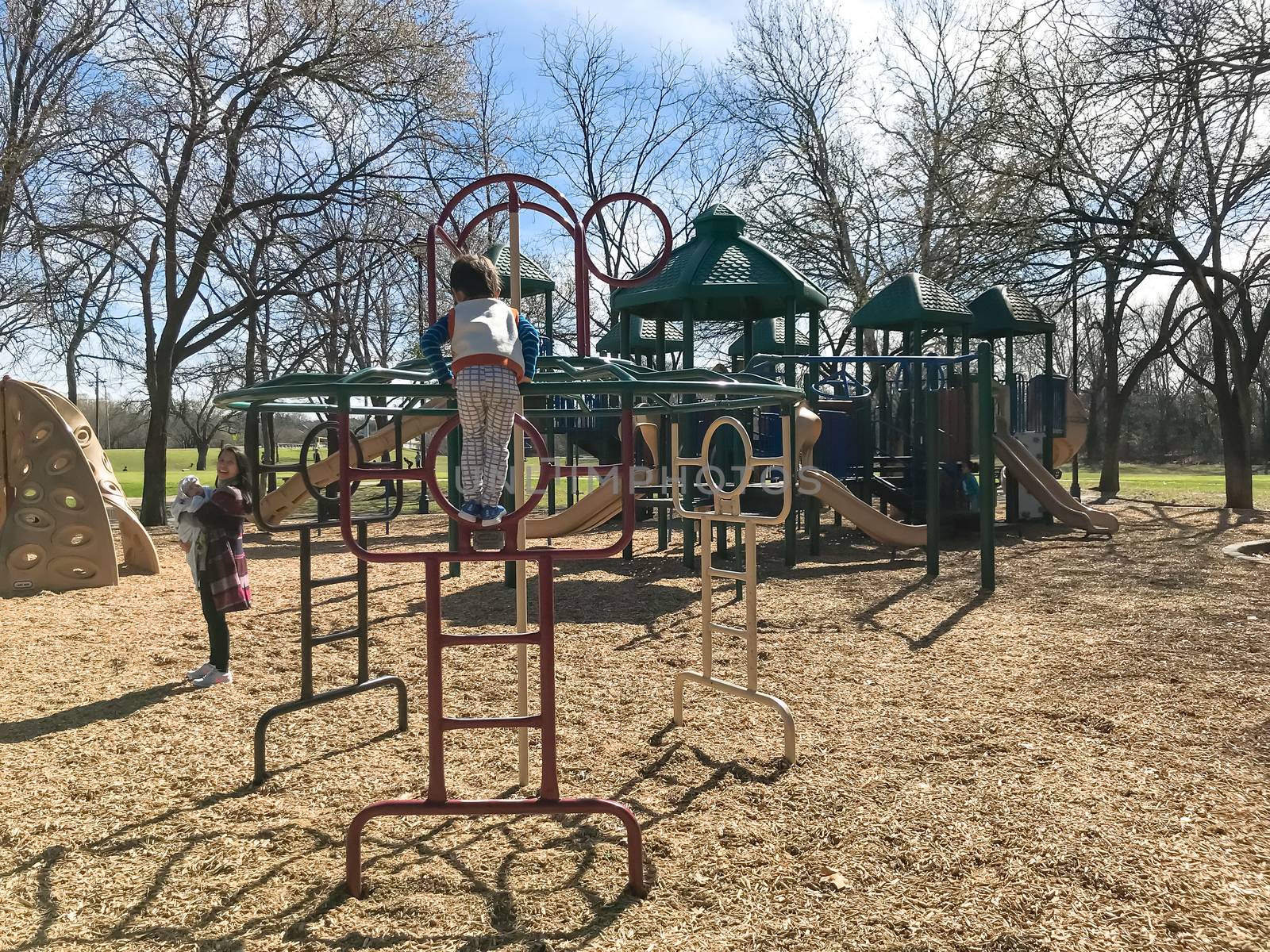 Healthy Asian toddler boy climbing structure at outdoor playground in Lewisville, Texas, USA. Sunny day of wintertime in North Texas