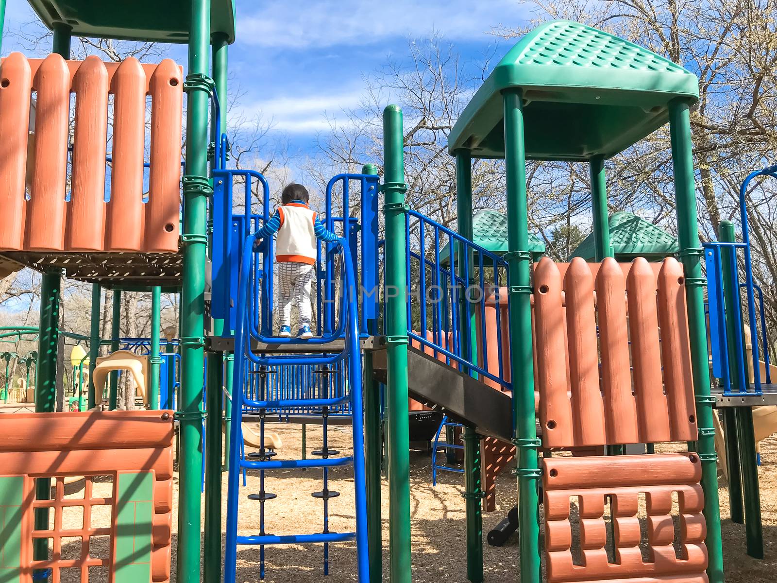 Rear view young Asian boy climbing structure at playground in wintertime by trongnguyen