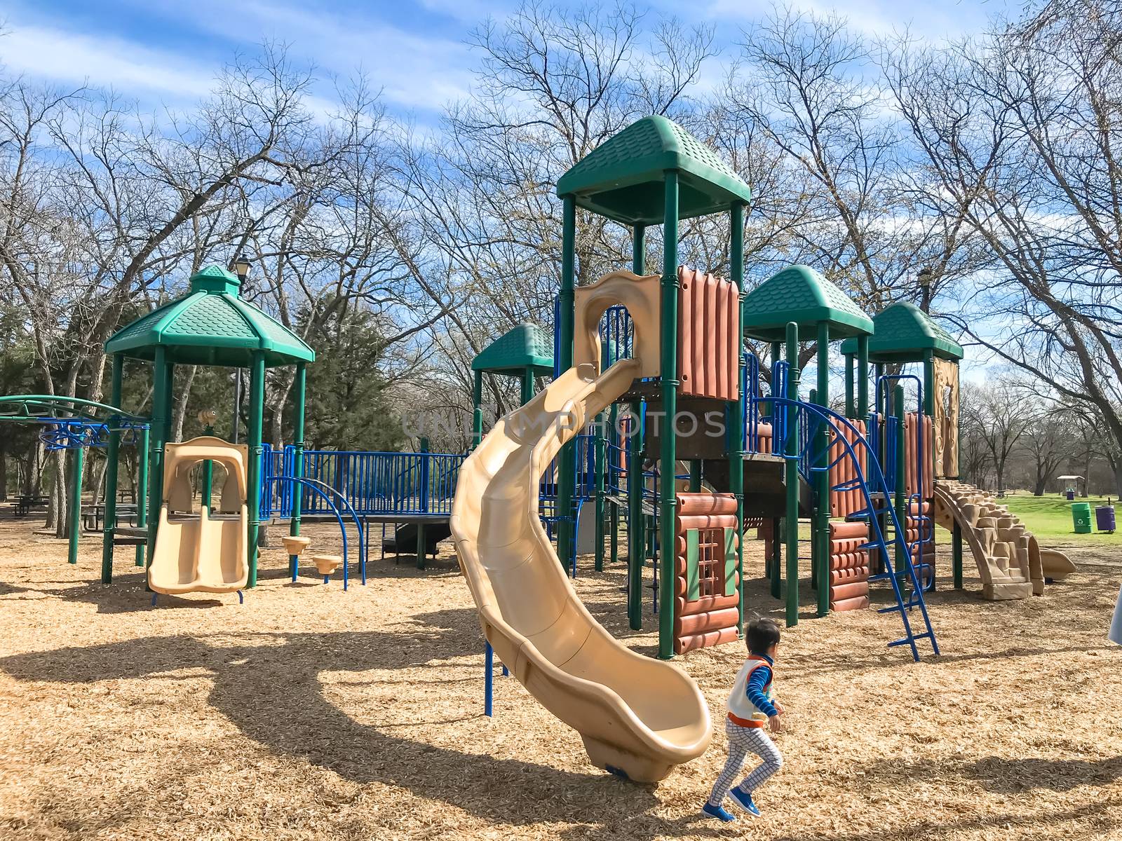 Rear view of active Asian boy running at playground during wintertime in Lewisville, Texas, USA.