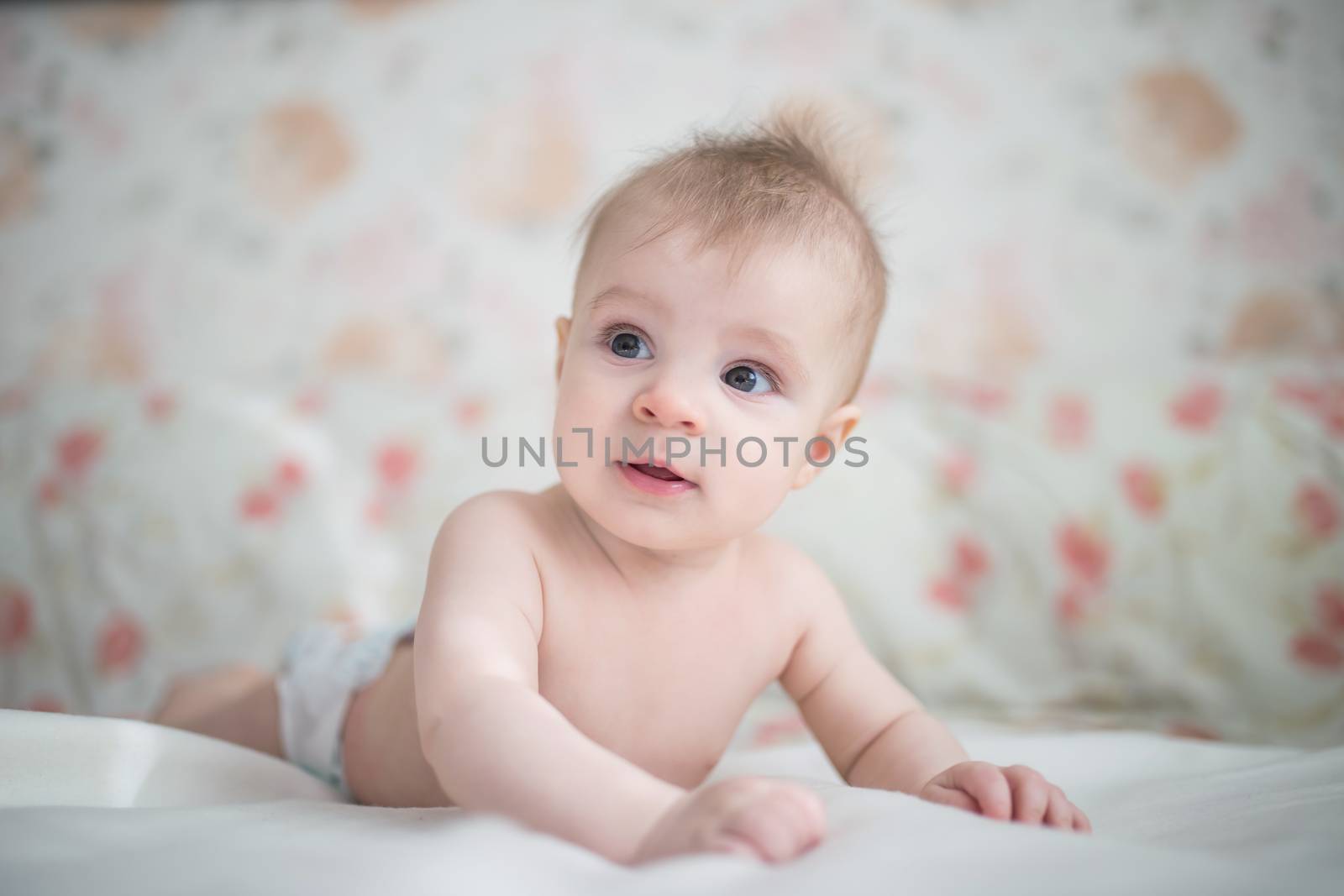 Curious baby boy lying in bed on white