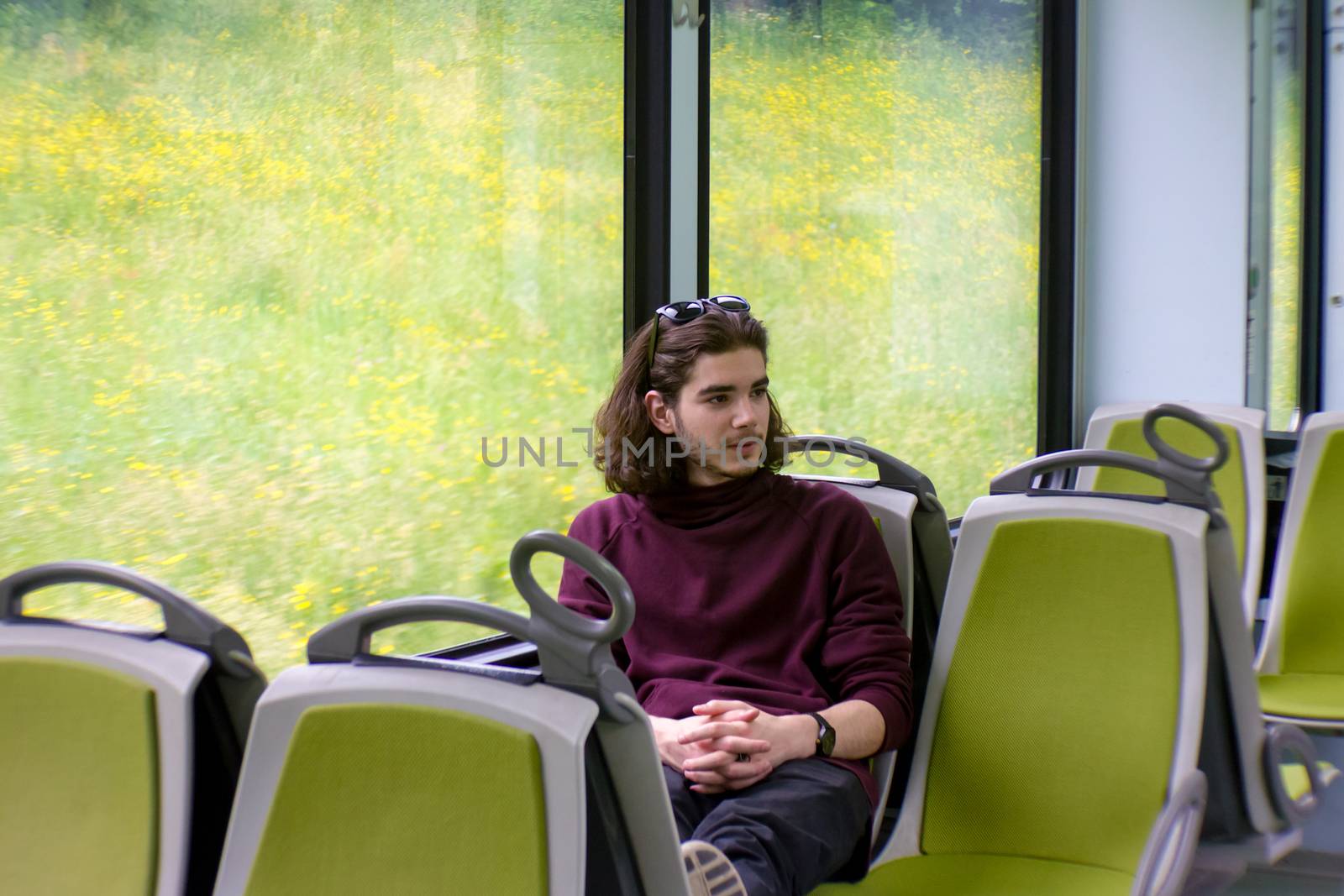 A handsome guy rides a suburban train, sits and looks out the window, outside the window is a blooming spring meadow.
