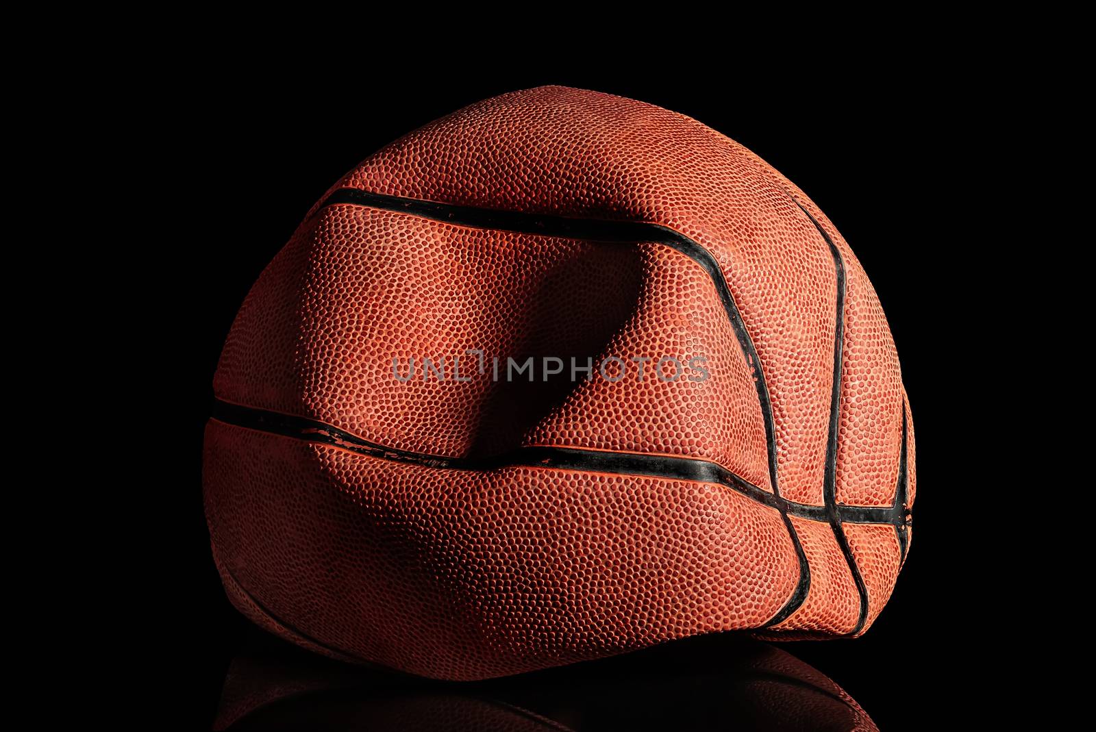 Deflated and rumpled old basketball ball. Black background. Reflection.