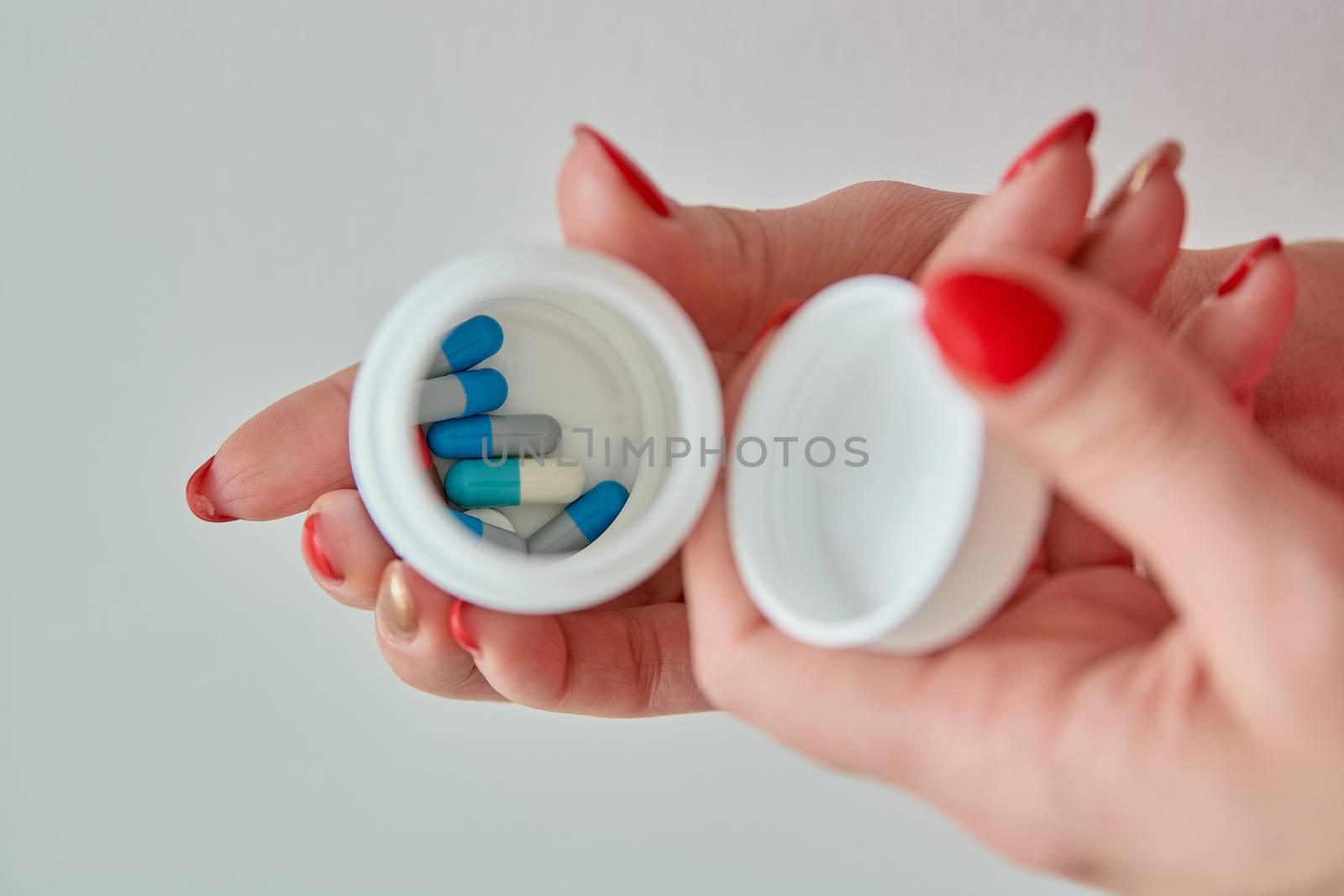Colored assorted pharmaceutical medicine pills, tablets and capsules in the box on female hand isoleted on white background. Close-up.
