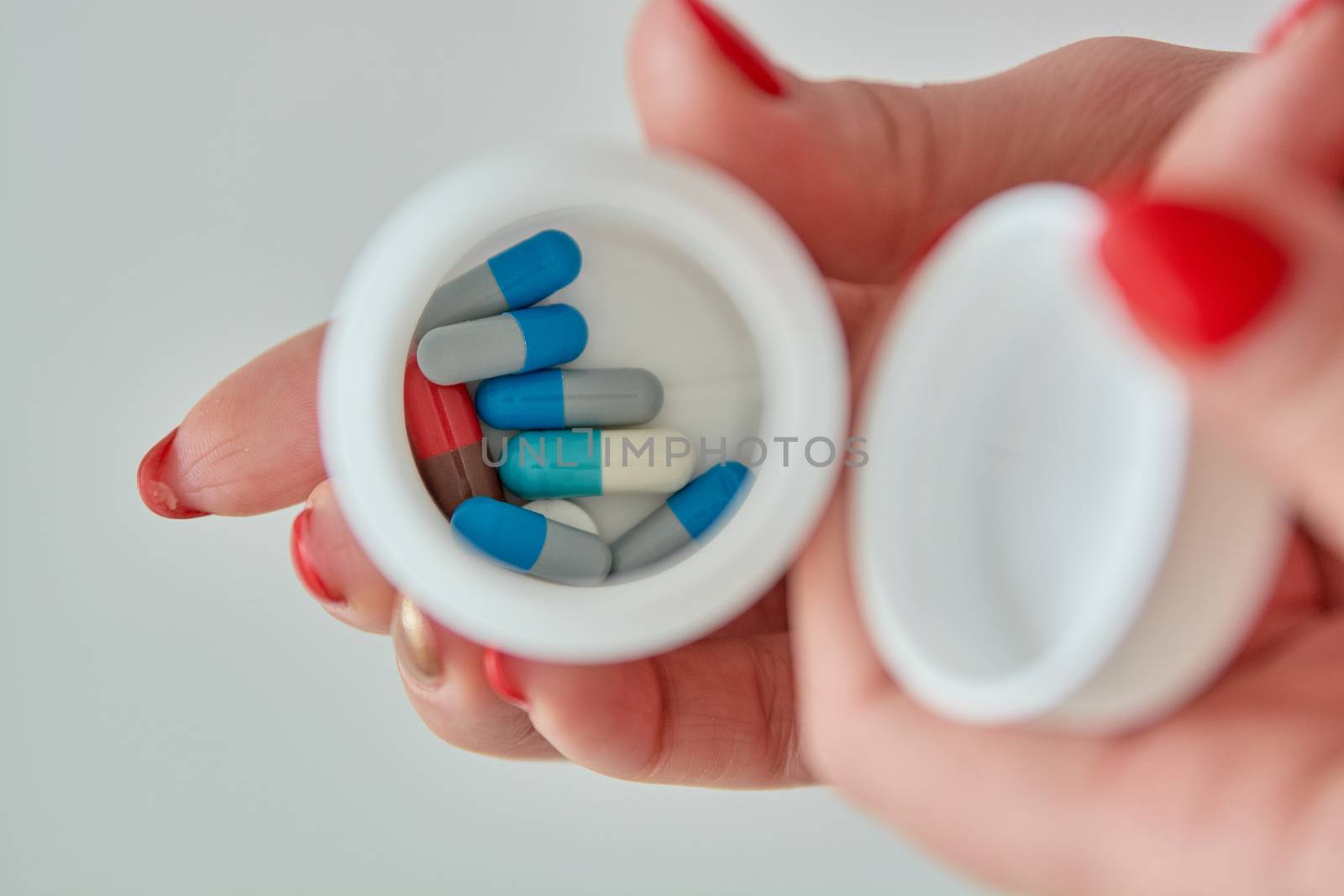Colored assorted pharmaceutical medicine pills, tablets and capsules in the box on female hand isoleted on white background. Close-up.