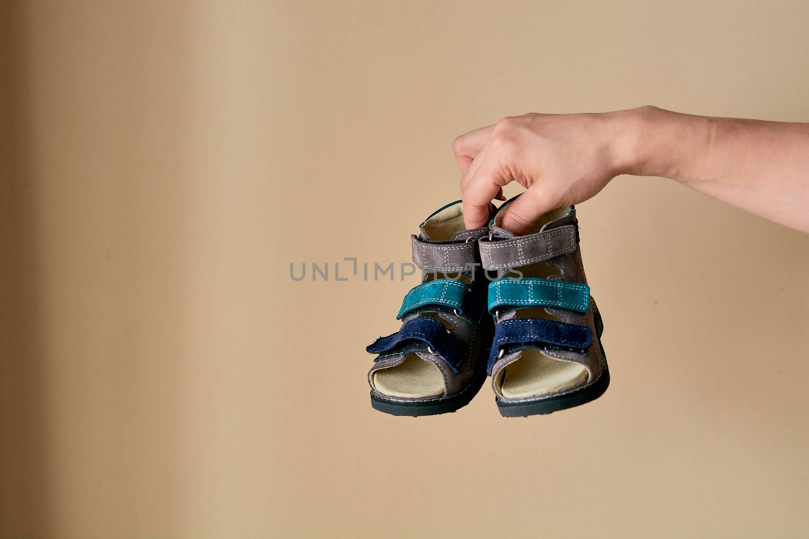 Female is holding close-up a special children's orthopedic shoe sandals made of genuine leather. Comfortable shoes isolated on light background with copyspace. Image suitable for advertising.